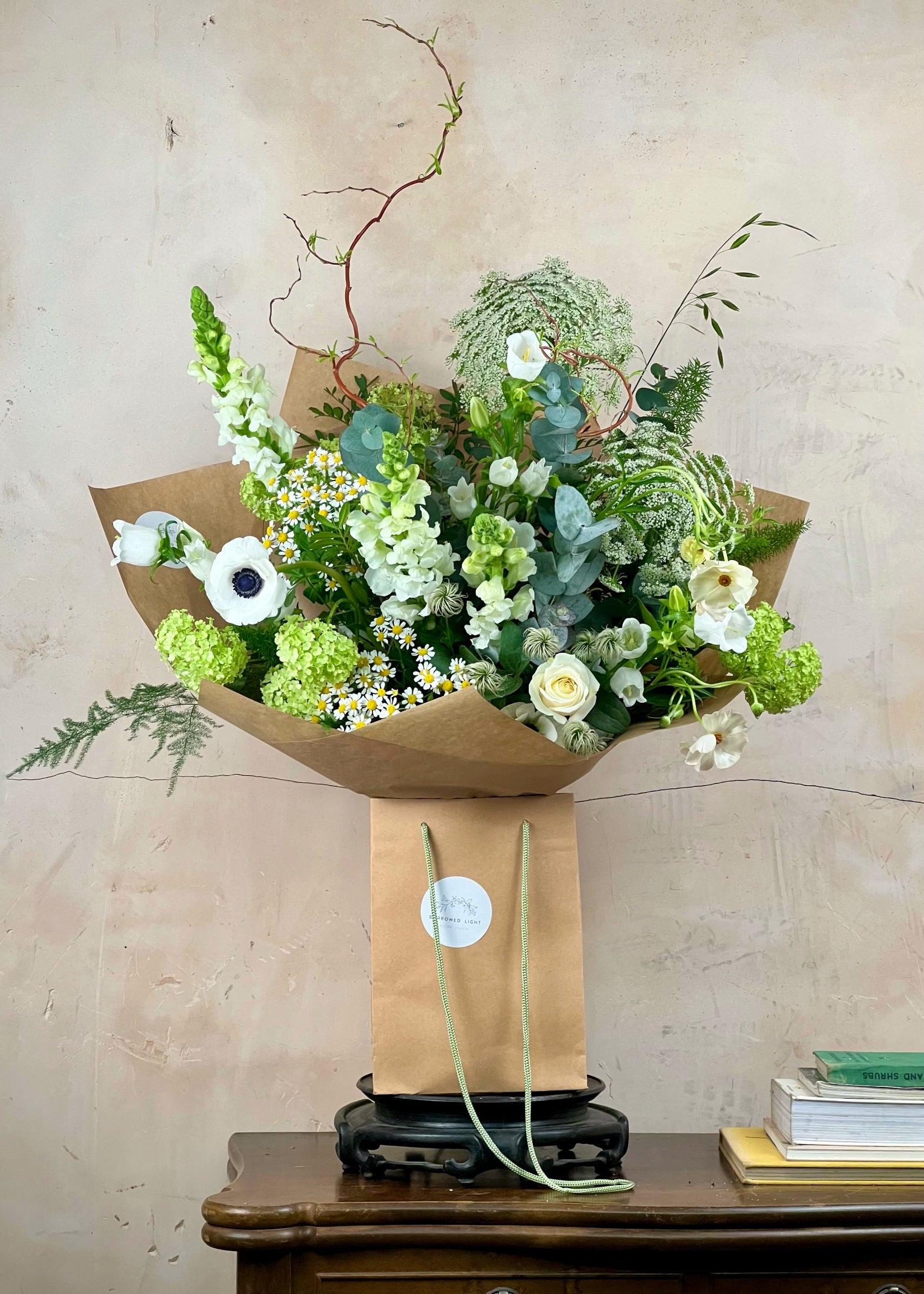 Bouquet of flowers wrapped in brown paper on a wooden table with a beige wall background