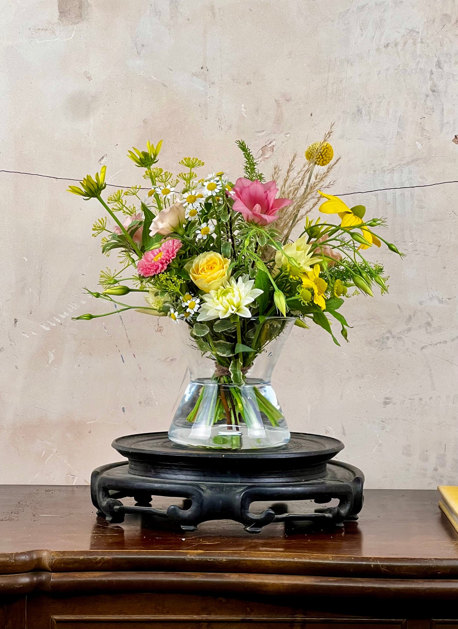 Bouquet of flowers in a clear vase on a wooden table with a textured wall background
