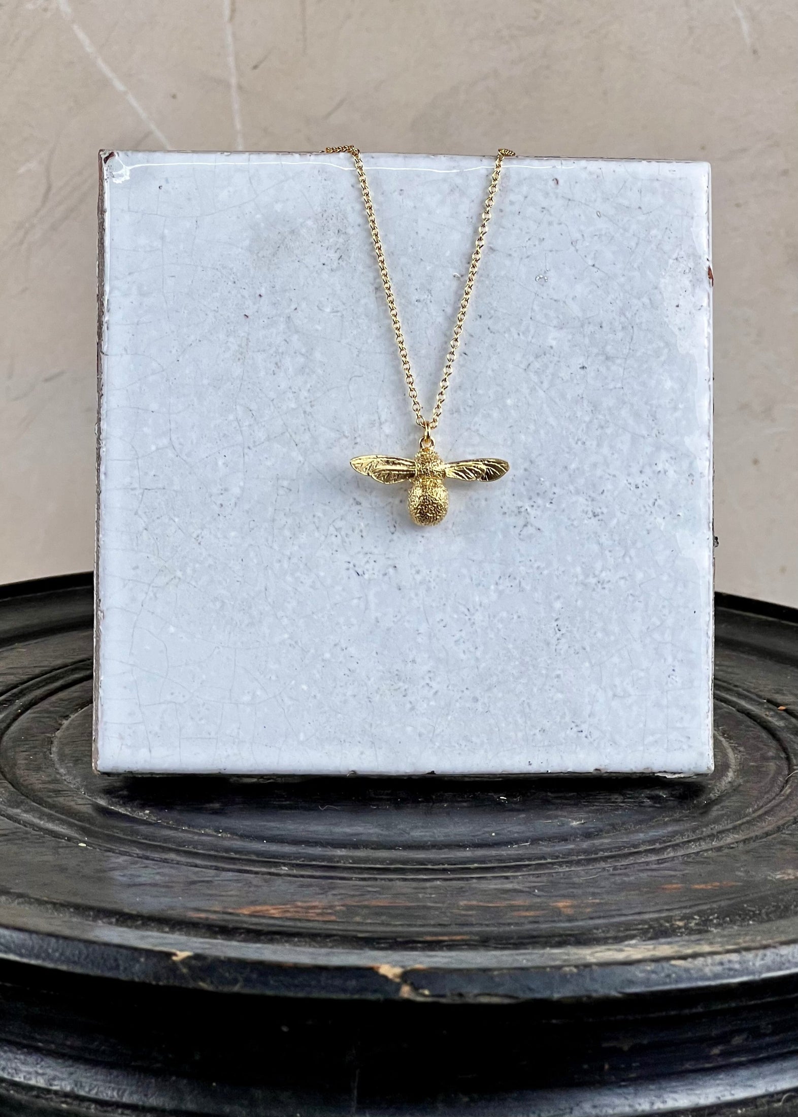 gold bee necklace on a white tile