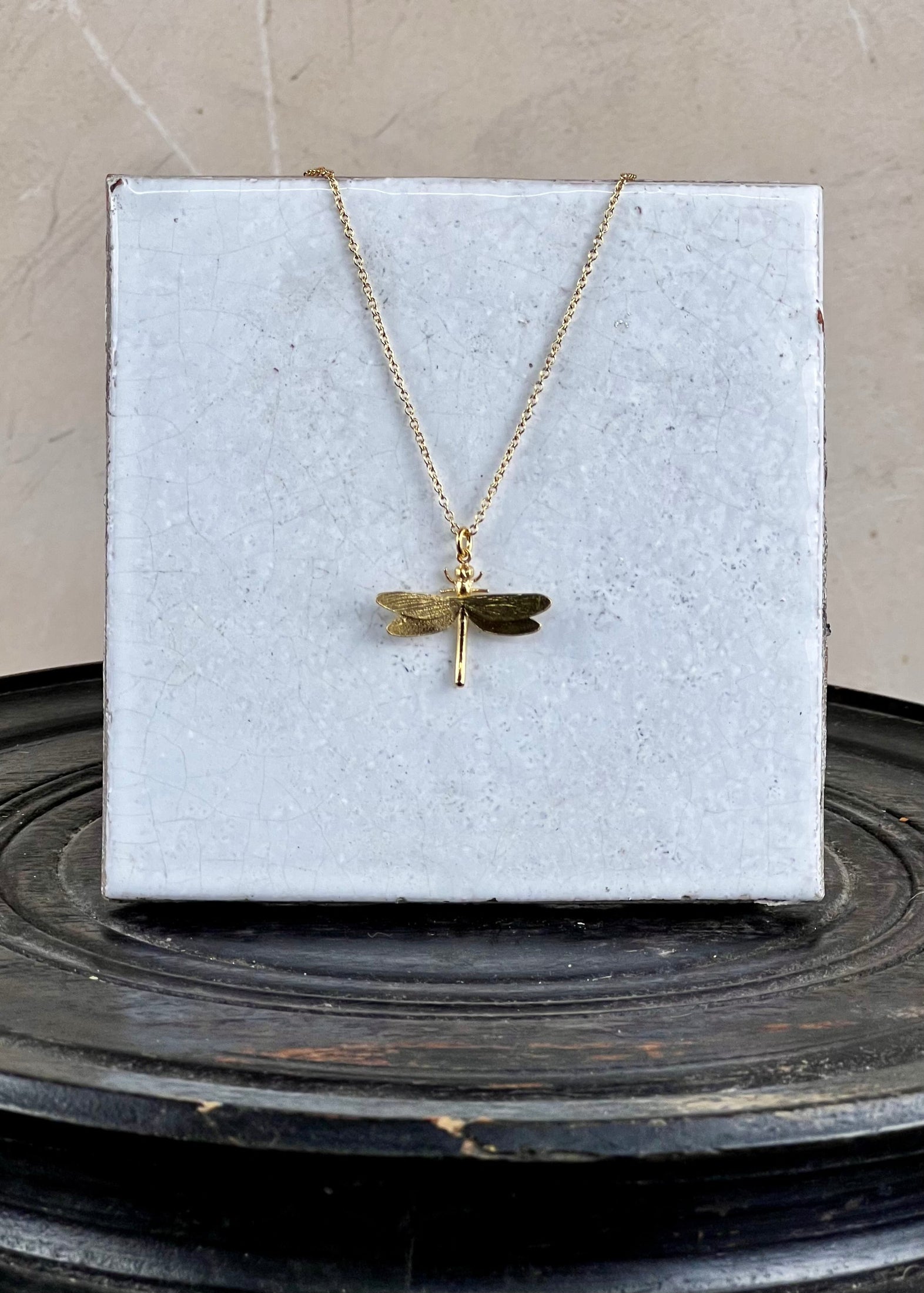 Gold dragonfly necklace on a white card with a gray background