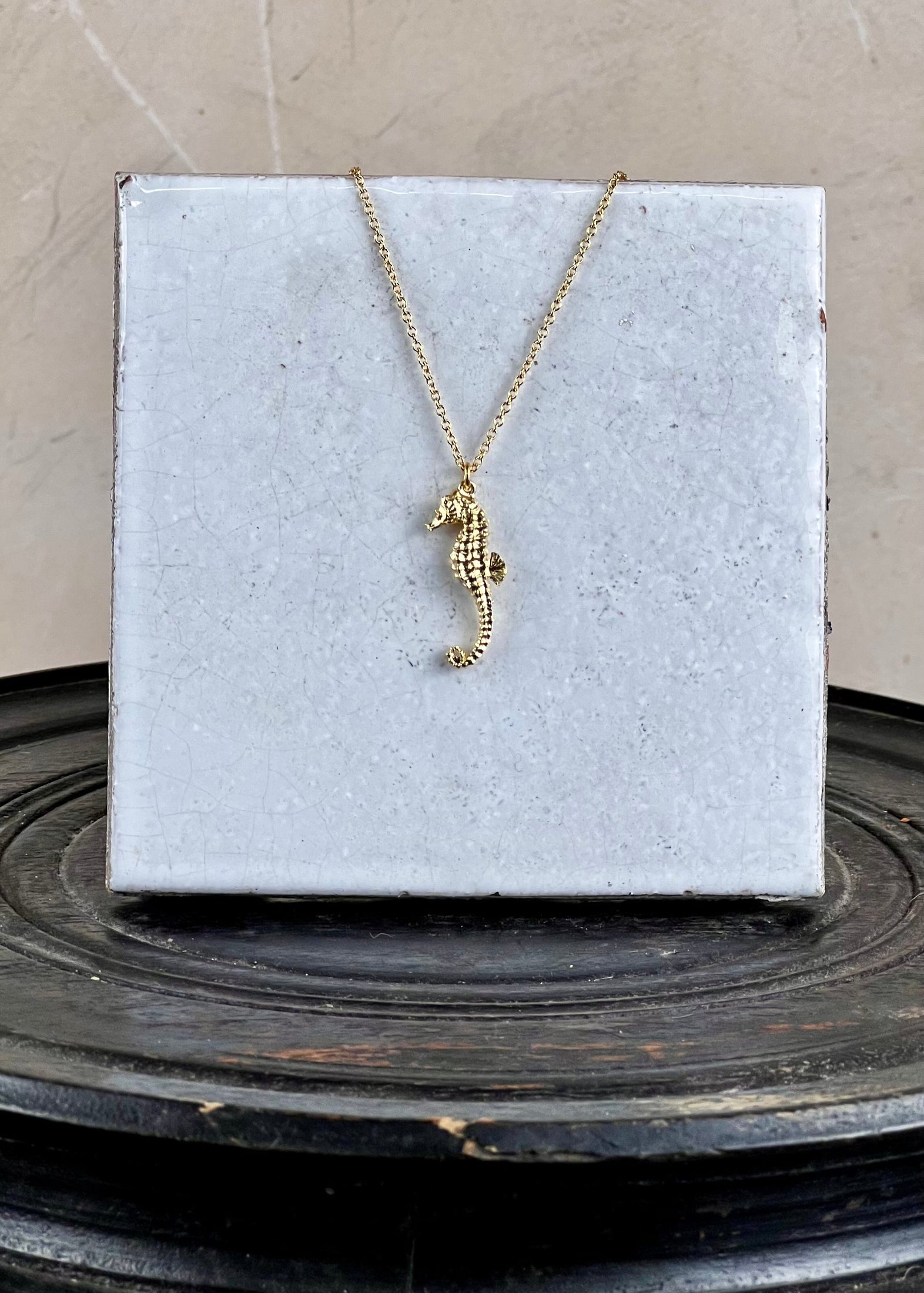 Gold seahorse necklace on a white card with a gray background