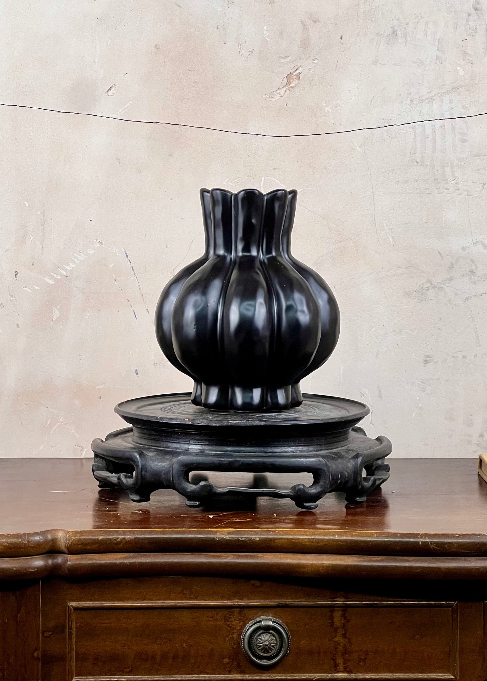 Black ceramic garlic bulb shaped vase on a wooden stand against a beige wall