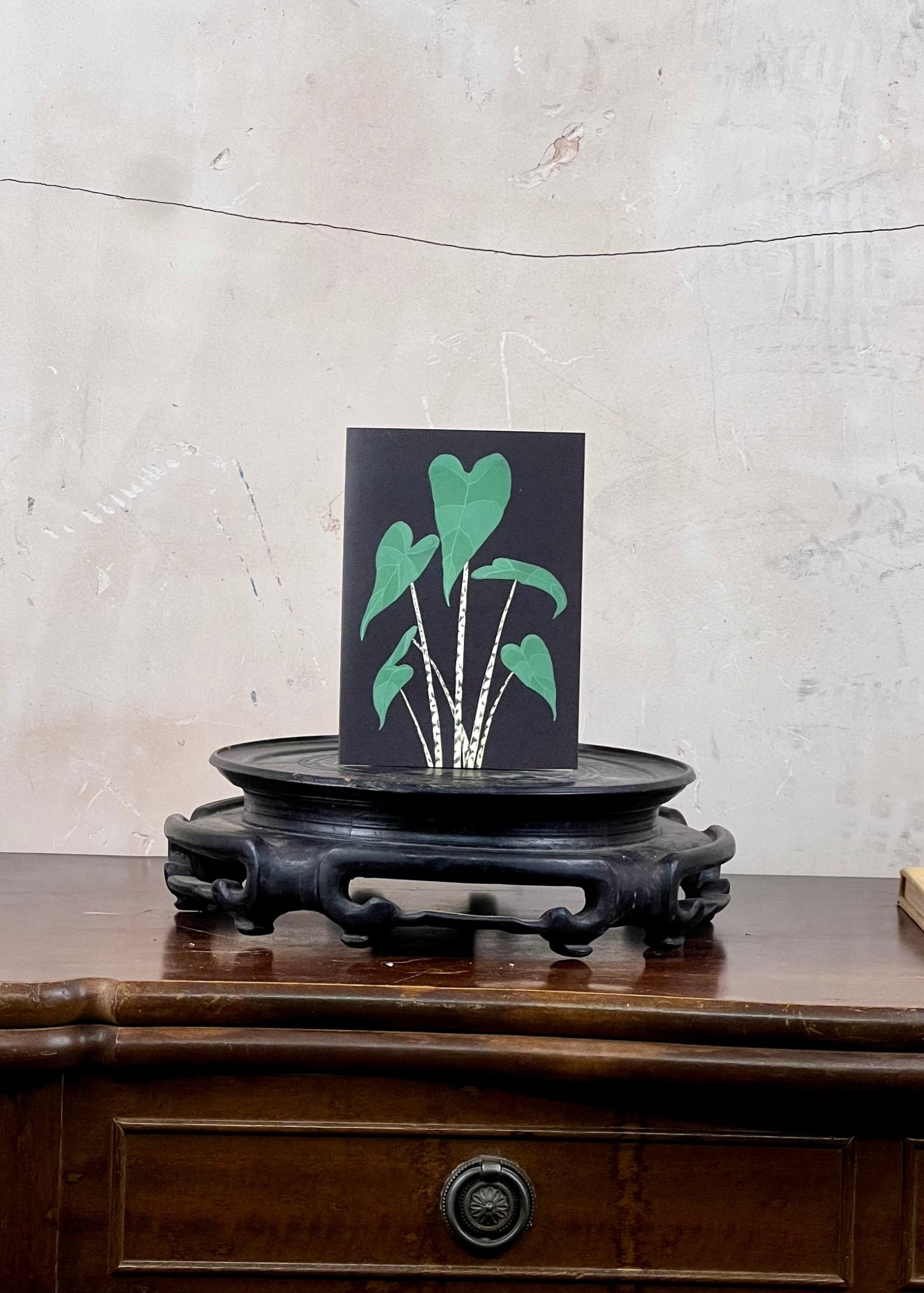 Card with green leaf design on a wooden stand against a textured wall.