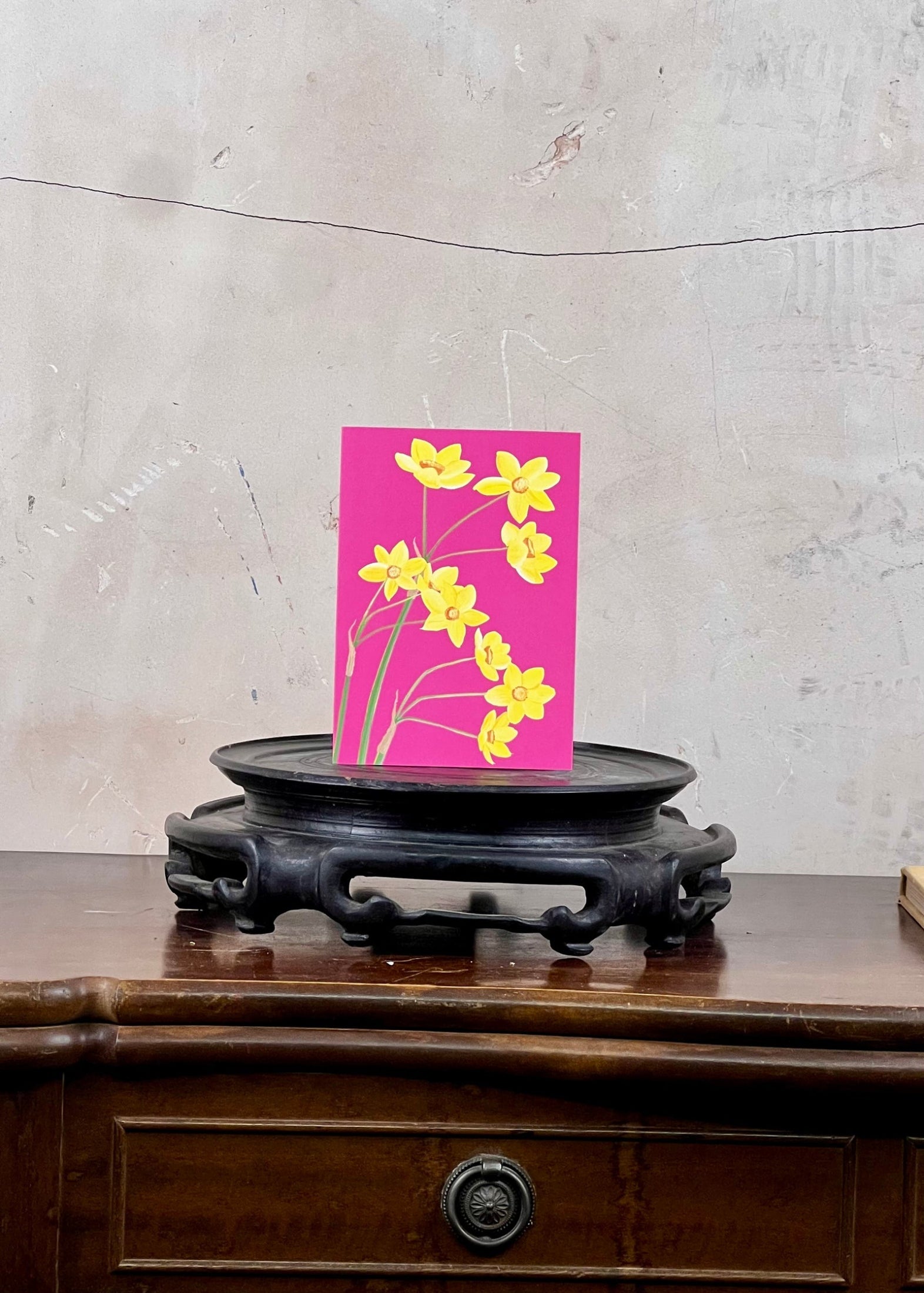 Card with yellow flowers on a pink background on a wooden surface with a textured wall.