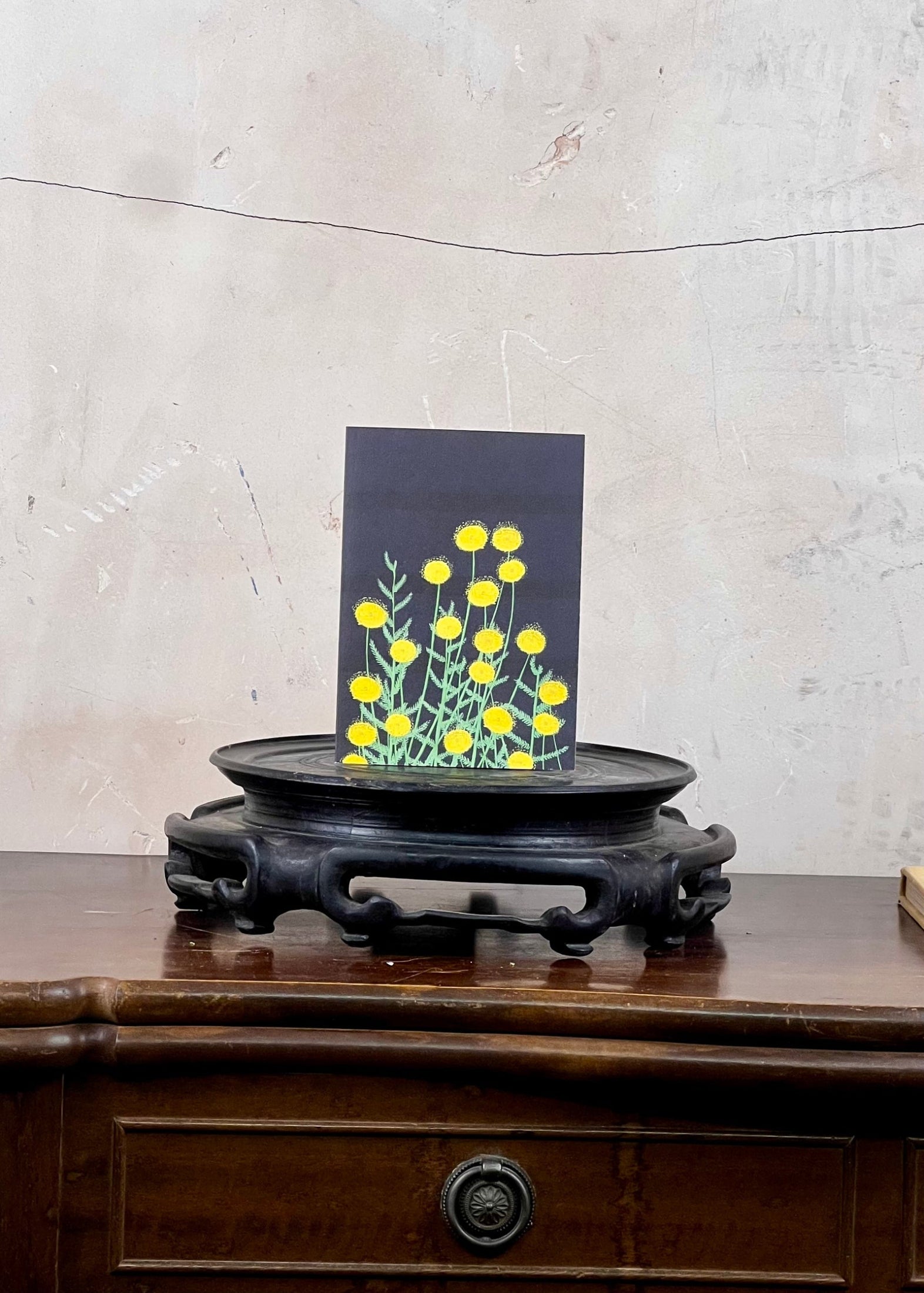 Card with yellow floral design on a wooden stand against a textured wall.