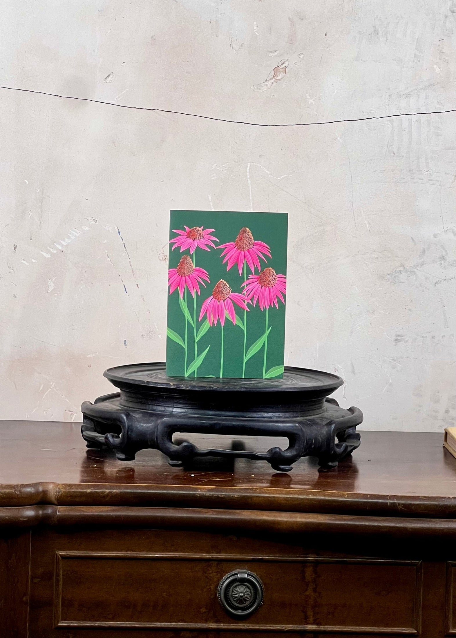 Card with pink flowers on a stand against a textured wall.