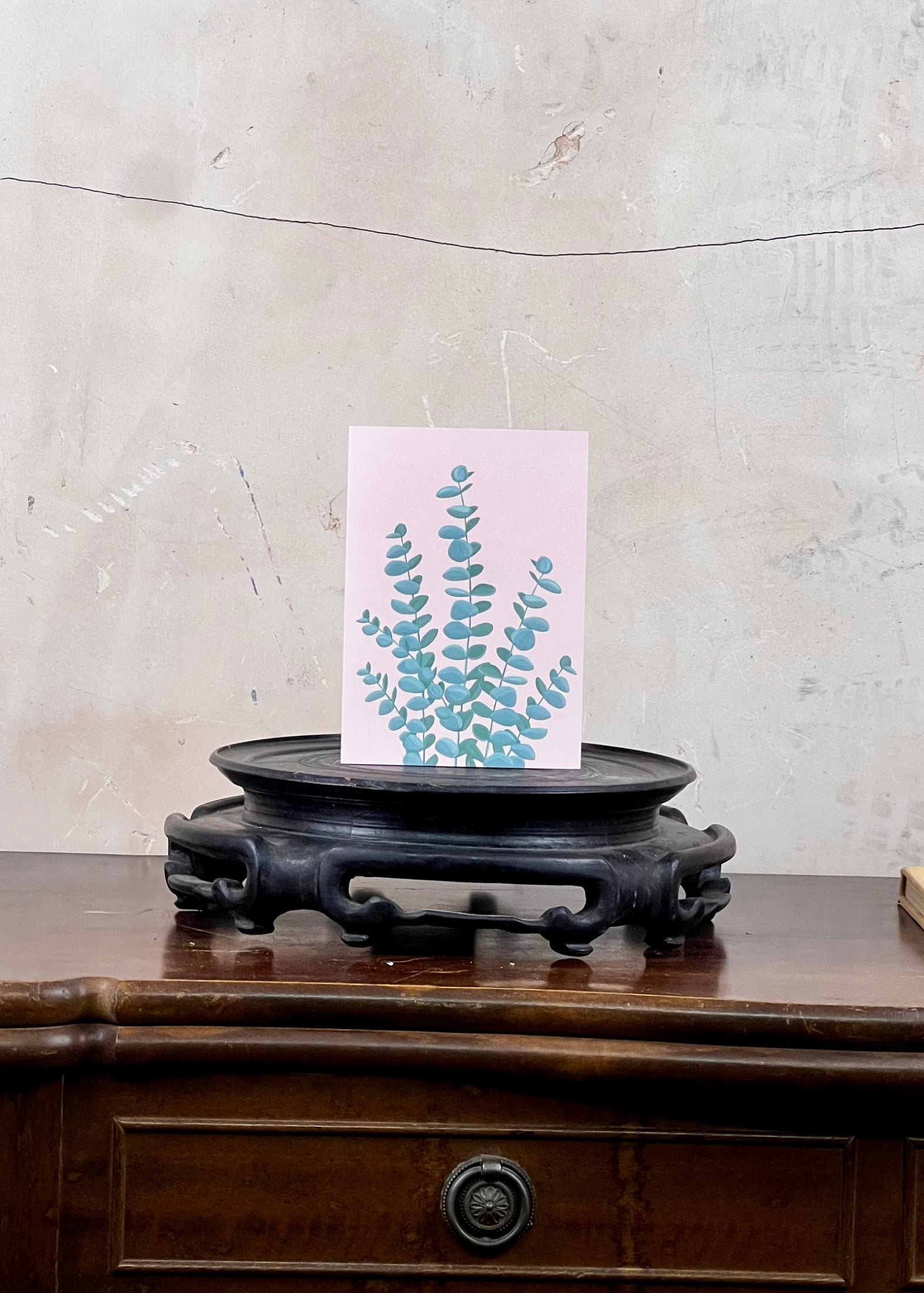 Card with floral design on a wooden stand against a textured wall.