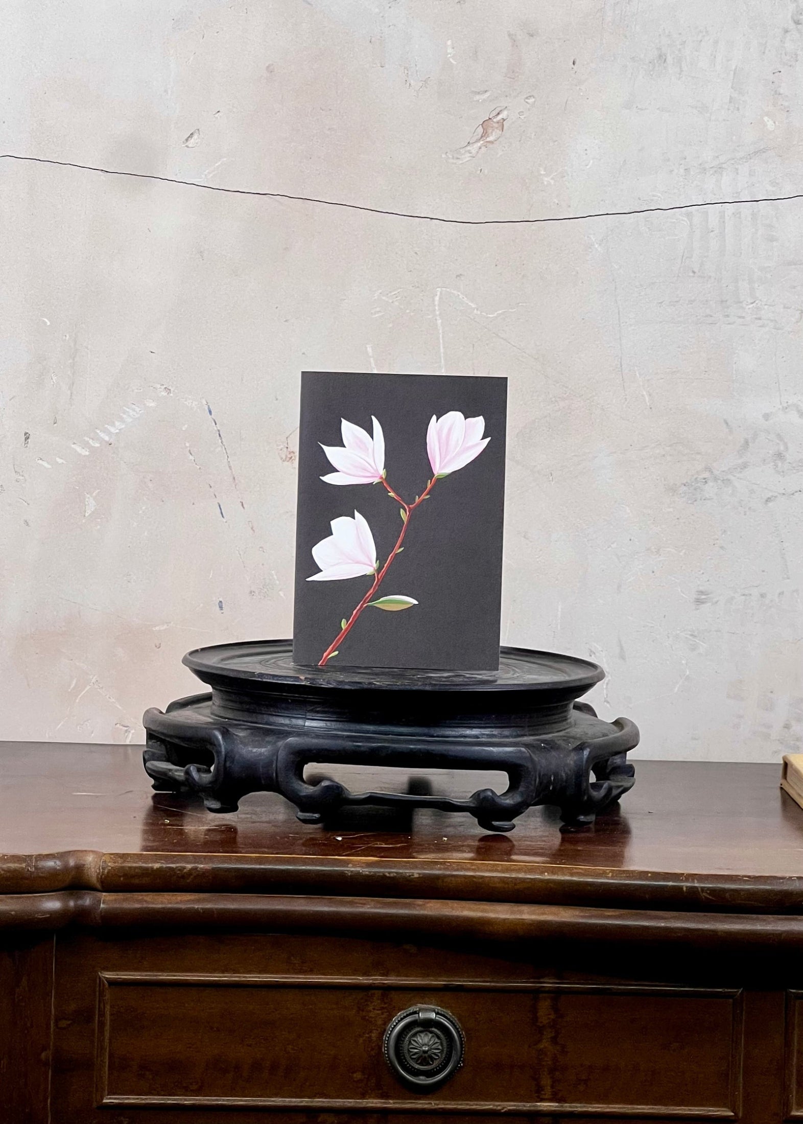 Card with floral design on a wooden stand against a textured wall.