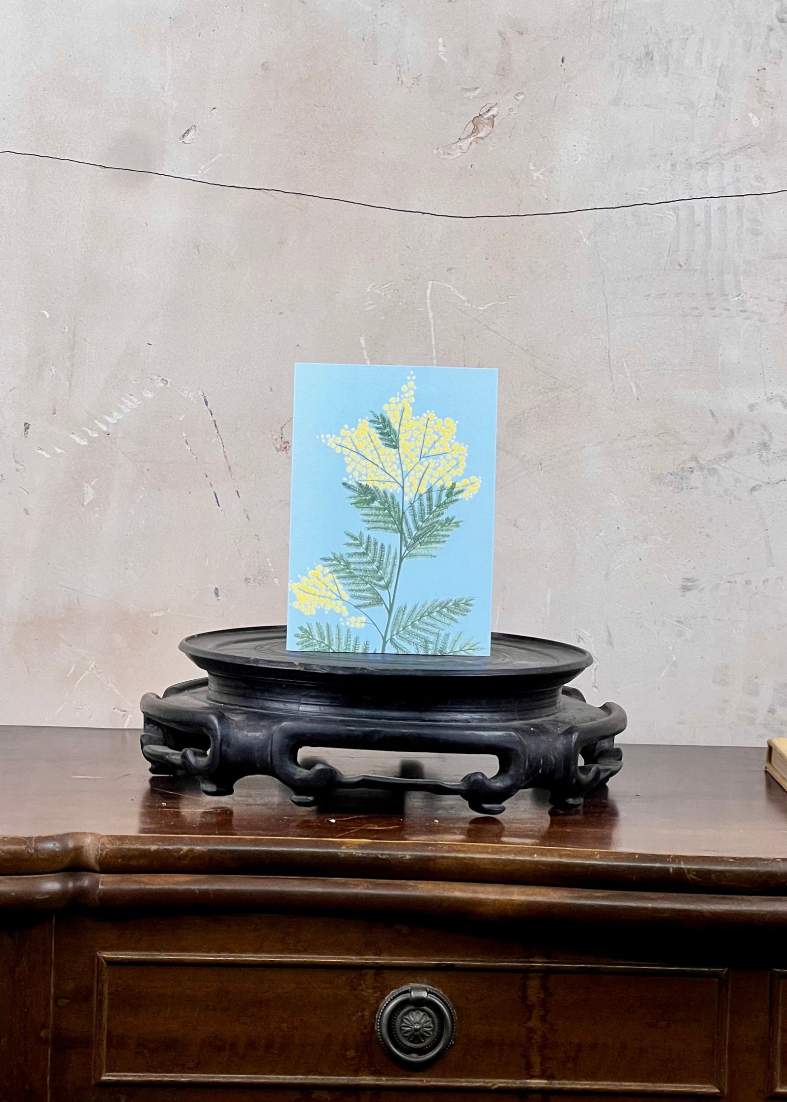 Card with floral design on a wooden stand against a textured wall.