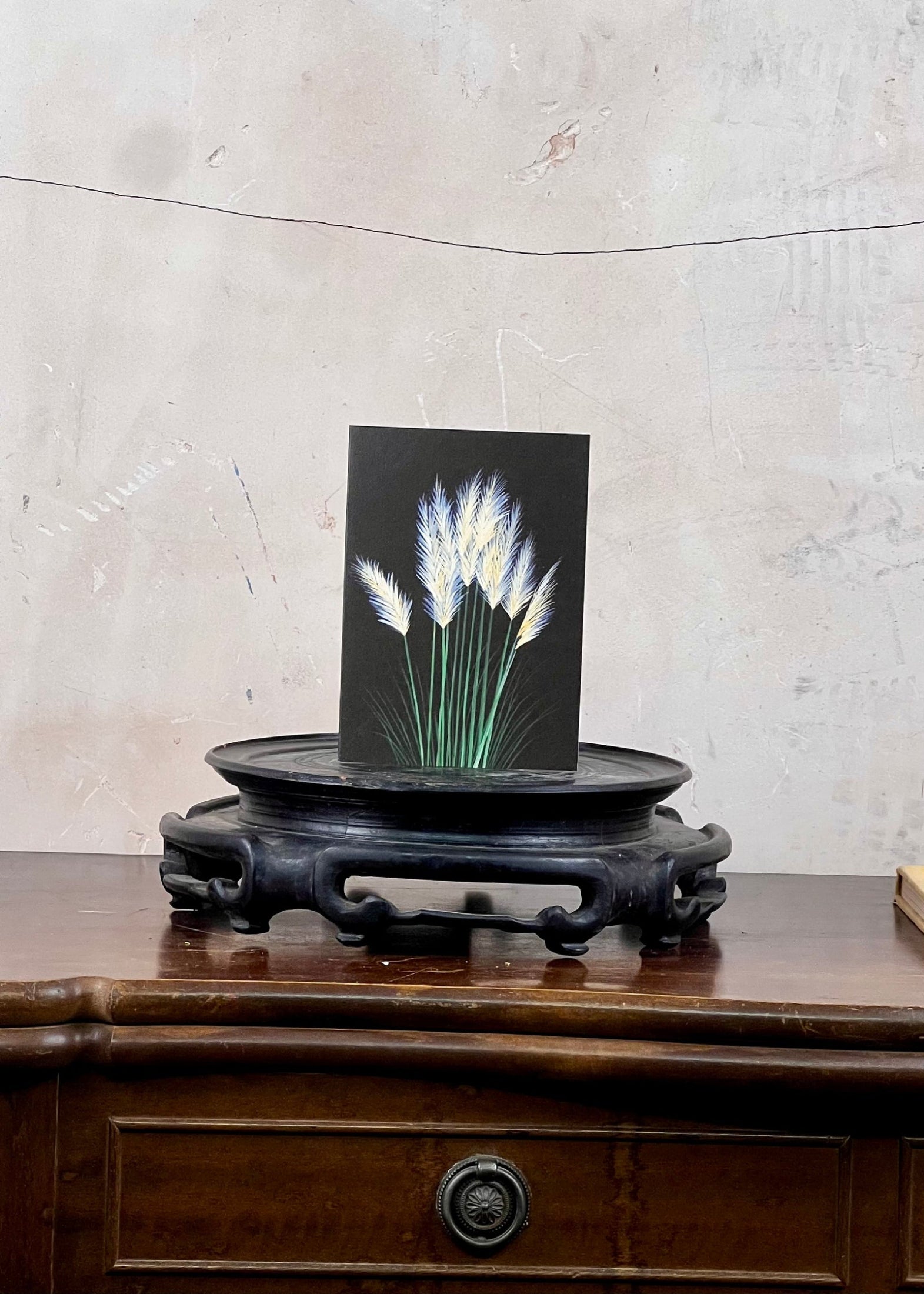 Card with floral design on a black stand on a wooden surface with a textured wall background
