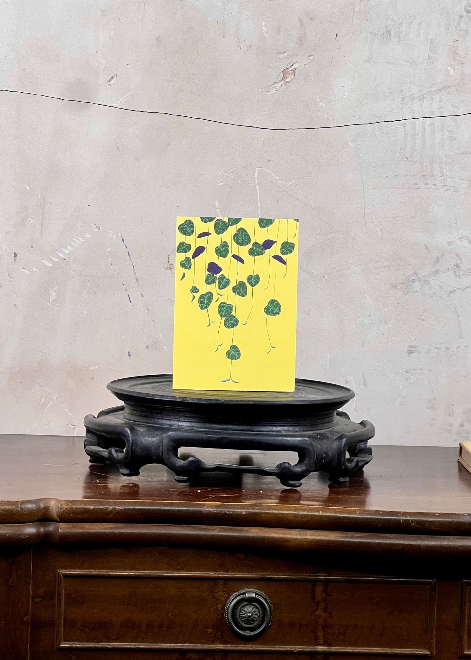 Yellow card with green floral design on a wooden stand against a textured wall.
