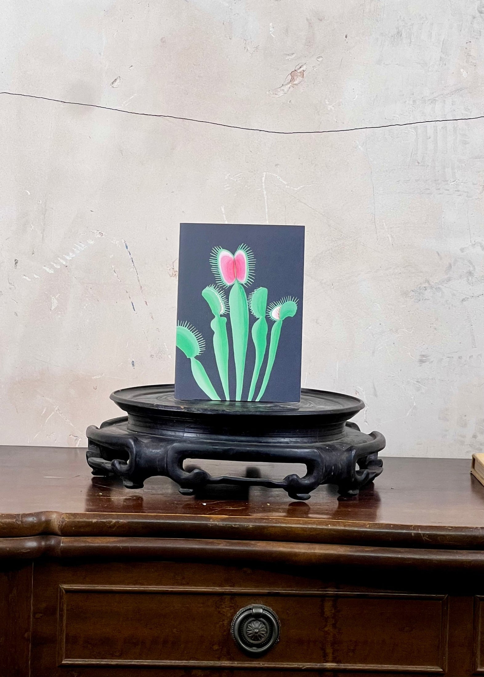 Card with a cactus design on a wooden stand against a textured wall.