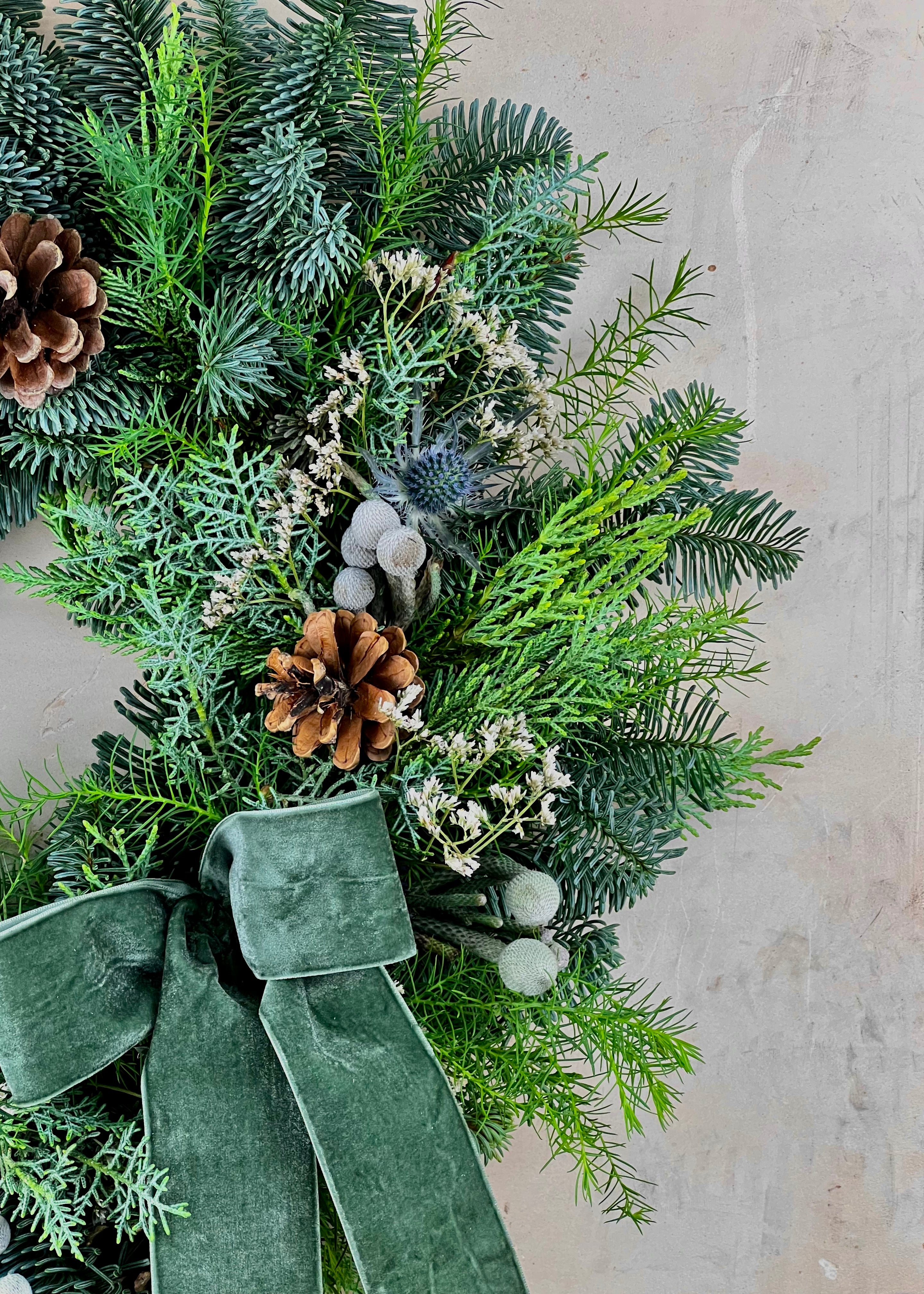 Decorative wreath with greenery, pinecones, and a green ribbon on a light background