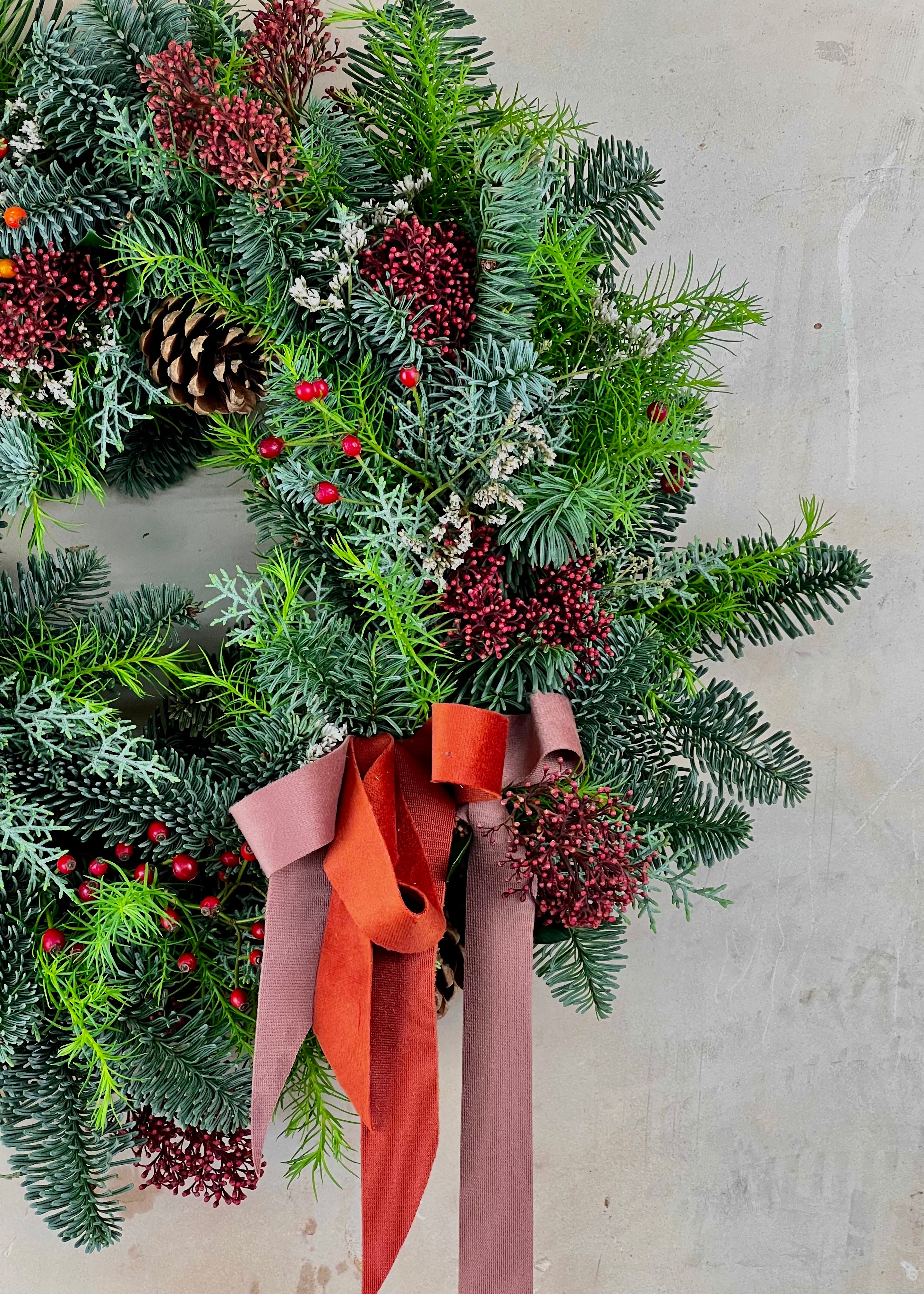 Christmas wreath with greenery, berries, and an orange ribbon on a light gray background