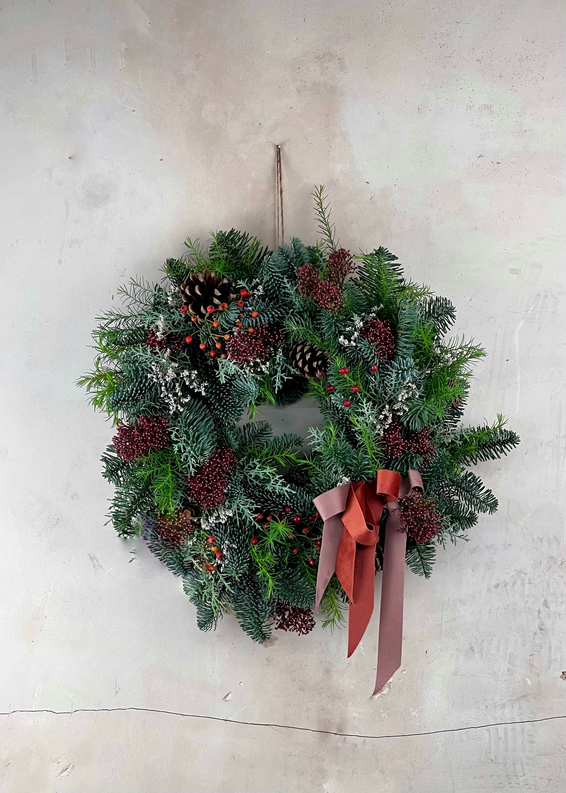 Classic Christmas wreath with greenery, berries, pinecones, rosehips and a pink ribbon on a light gray background