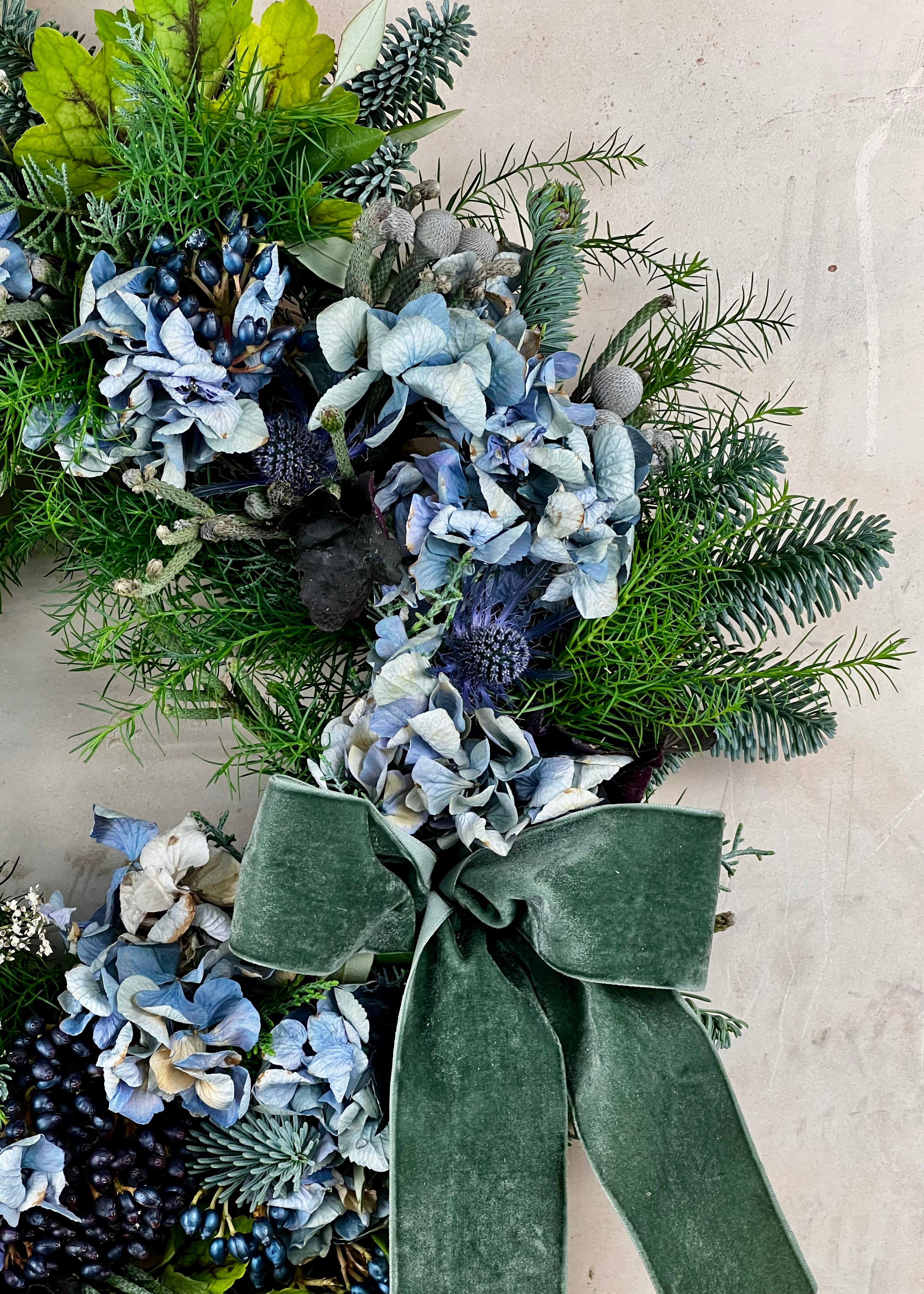 Decorative wreath with greenery and blue flowers on a light background