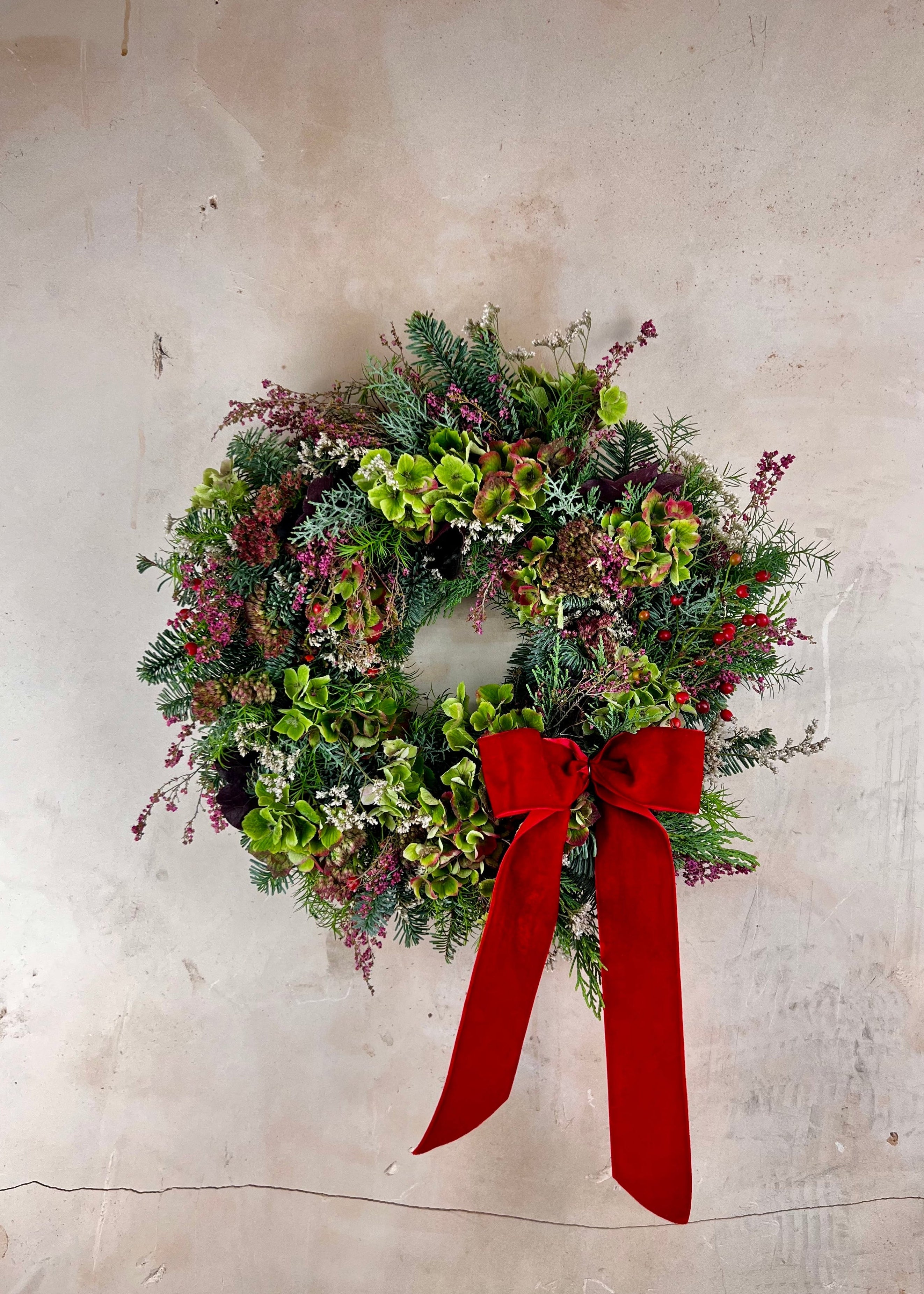 Delux Christmas wreath with hydrangea, rosehips, heather and a red bow on a textured wall