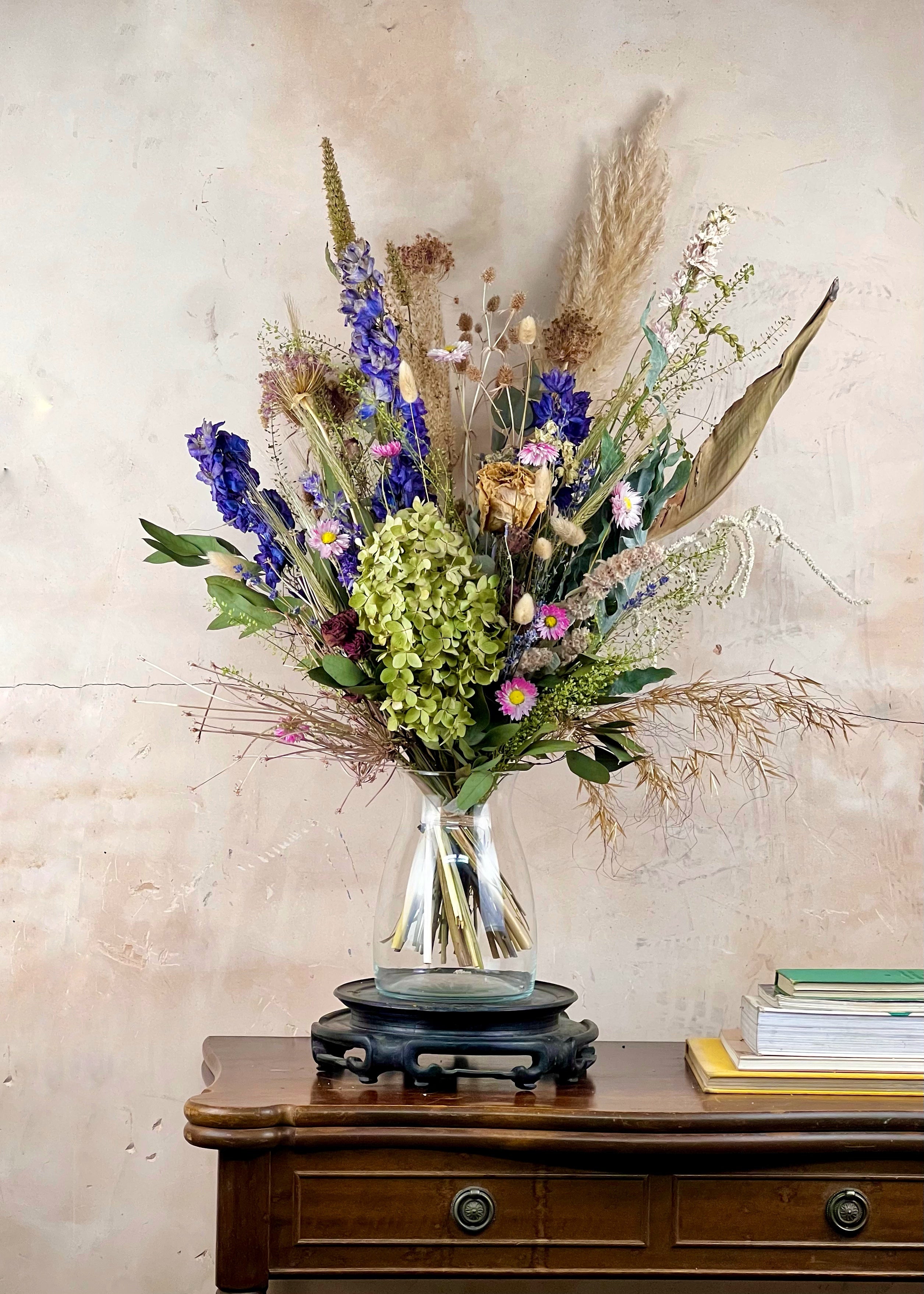 Bouquet of dried flowers in a clear vase on a wooden surface with a textured wall background