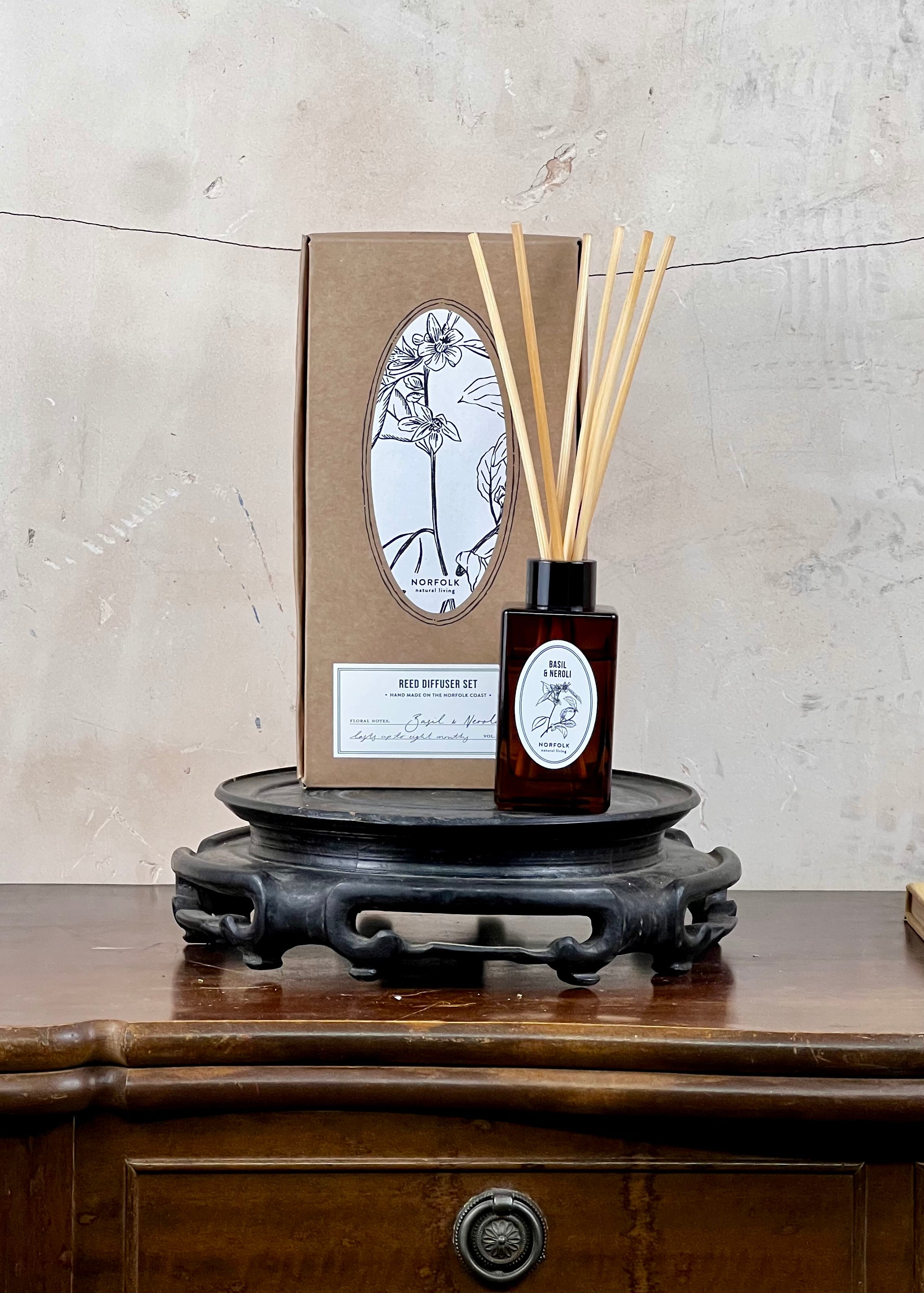 Reed diffuser set with packaging on a wooden surface against a concrete wall.