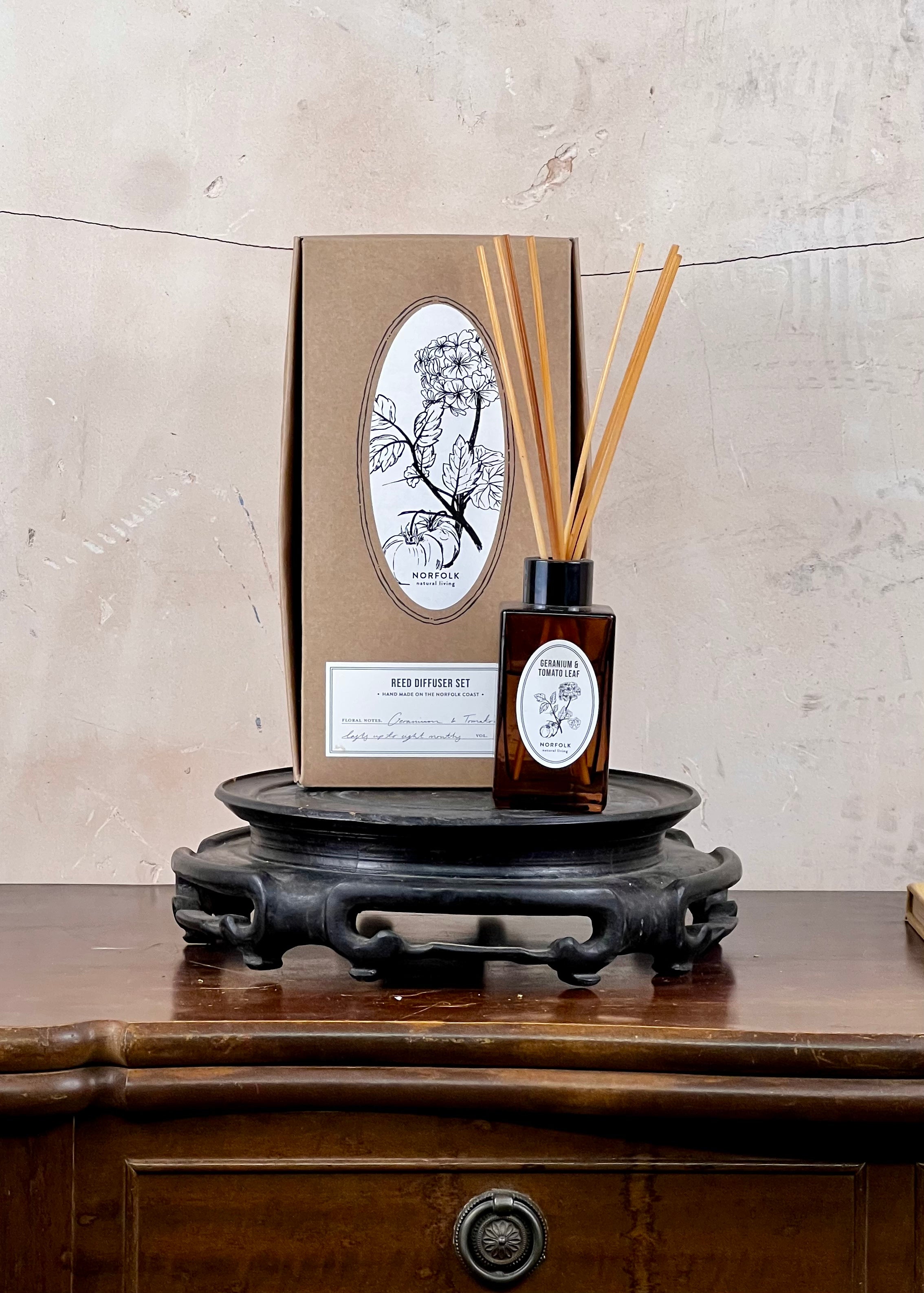 Reed diffuser set with bottle and sticks on a wooden stand against a neutral background