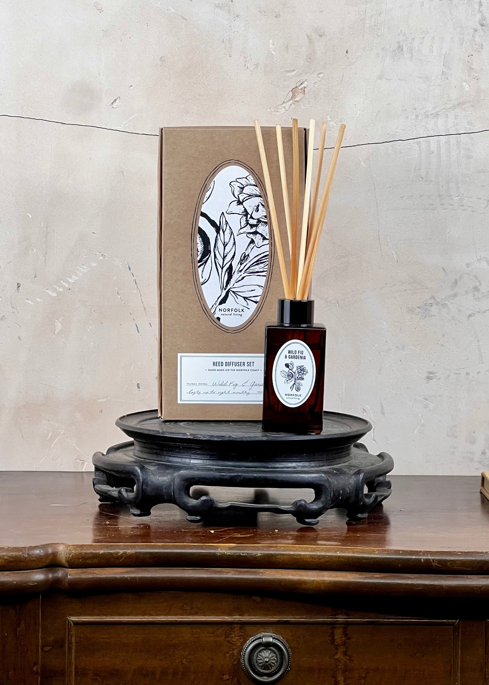 Diffuser bottle with reeds and packaging on a wooden surface with a textured wall background