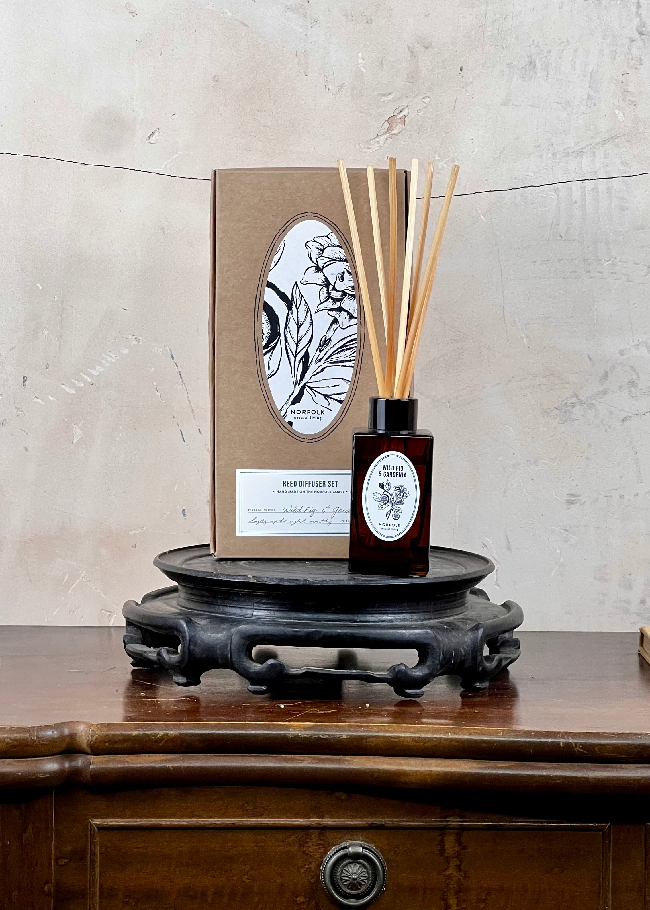 Diffuser bottle with reeds and packaging on a wooden surface with a textured wall background