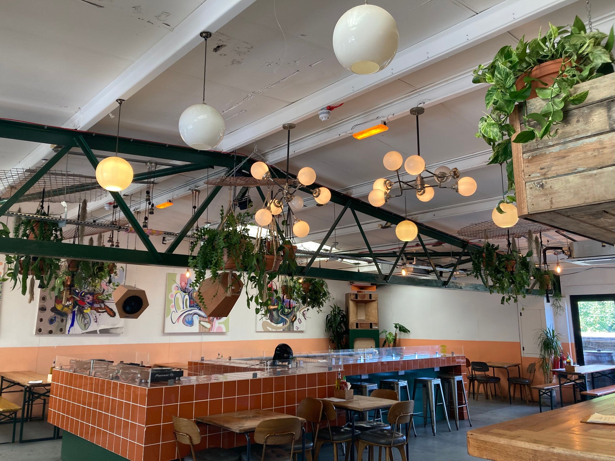 Modern restaurant interior with hanging lights, plants, and tables.