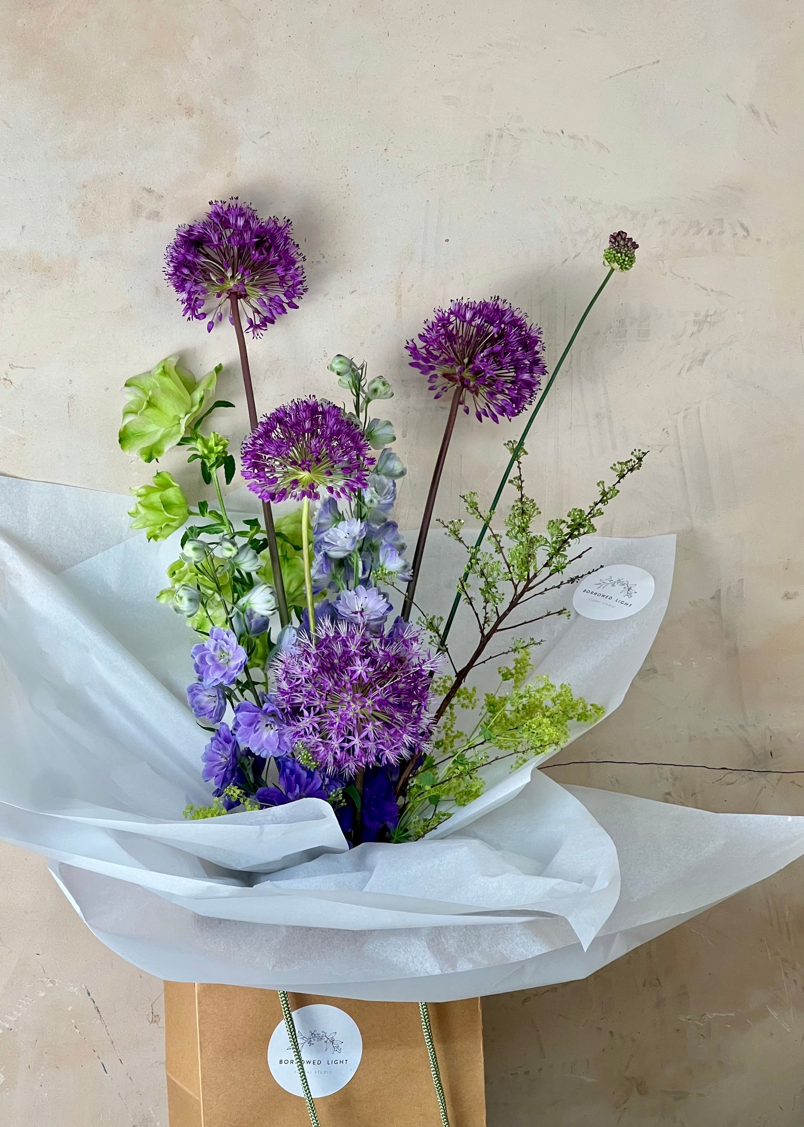Bouquet of purple and green flowers wrapped in white paper on a beige background