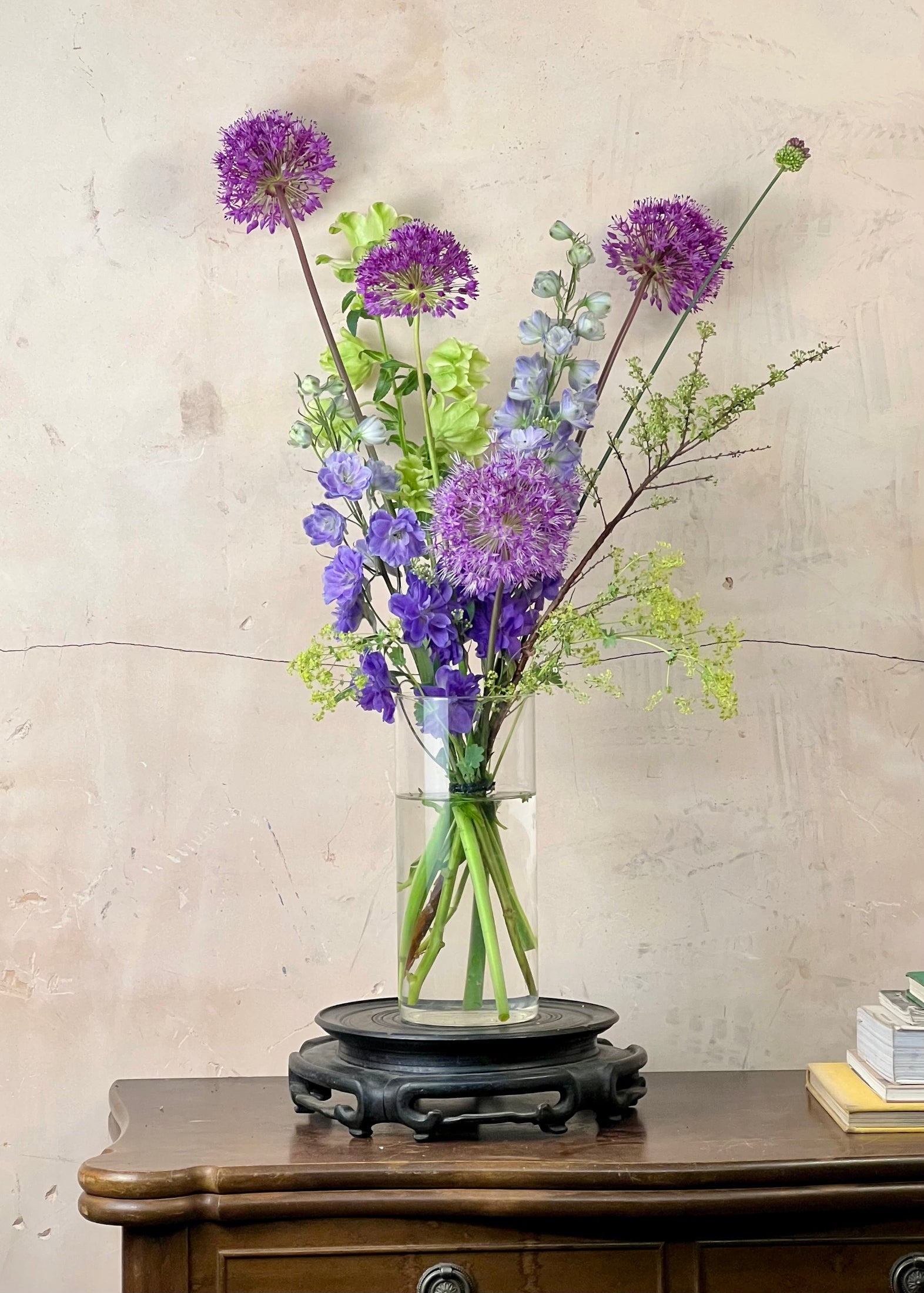 Vase with purple and green flowers on a wooden table against a beige wall