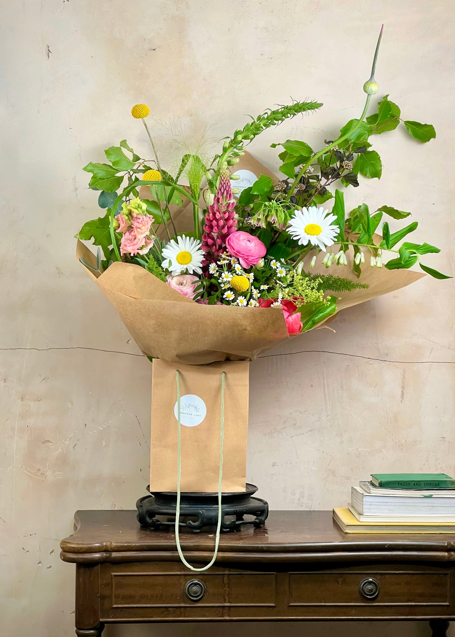 Bouquet of flowers wrapped in brown paper on a wooden table with a beige wall background