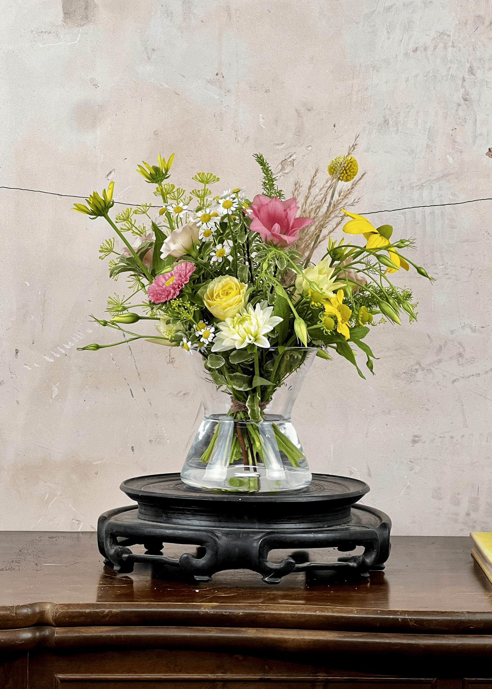 Bouquet of flowers included in a clear vase on a wooden table with a textured wall background