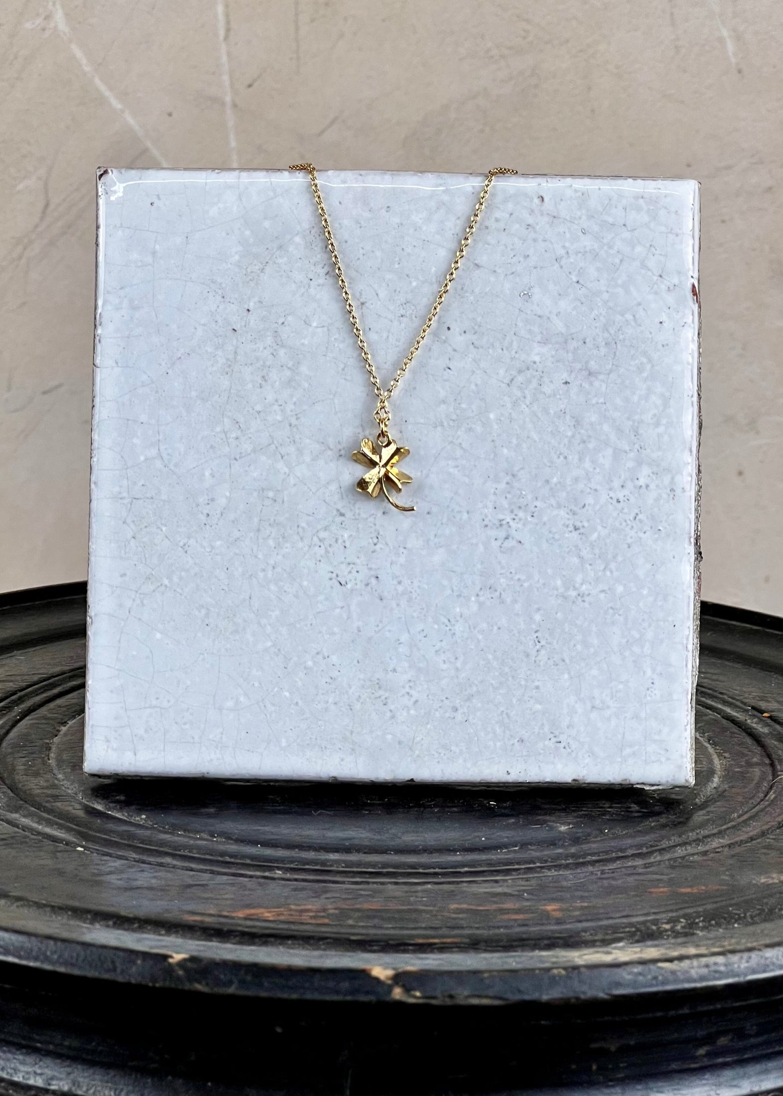 Gold necklace with a clover pendant on a white card against a beige background