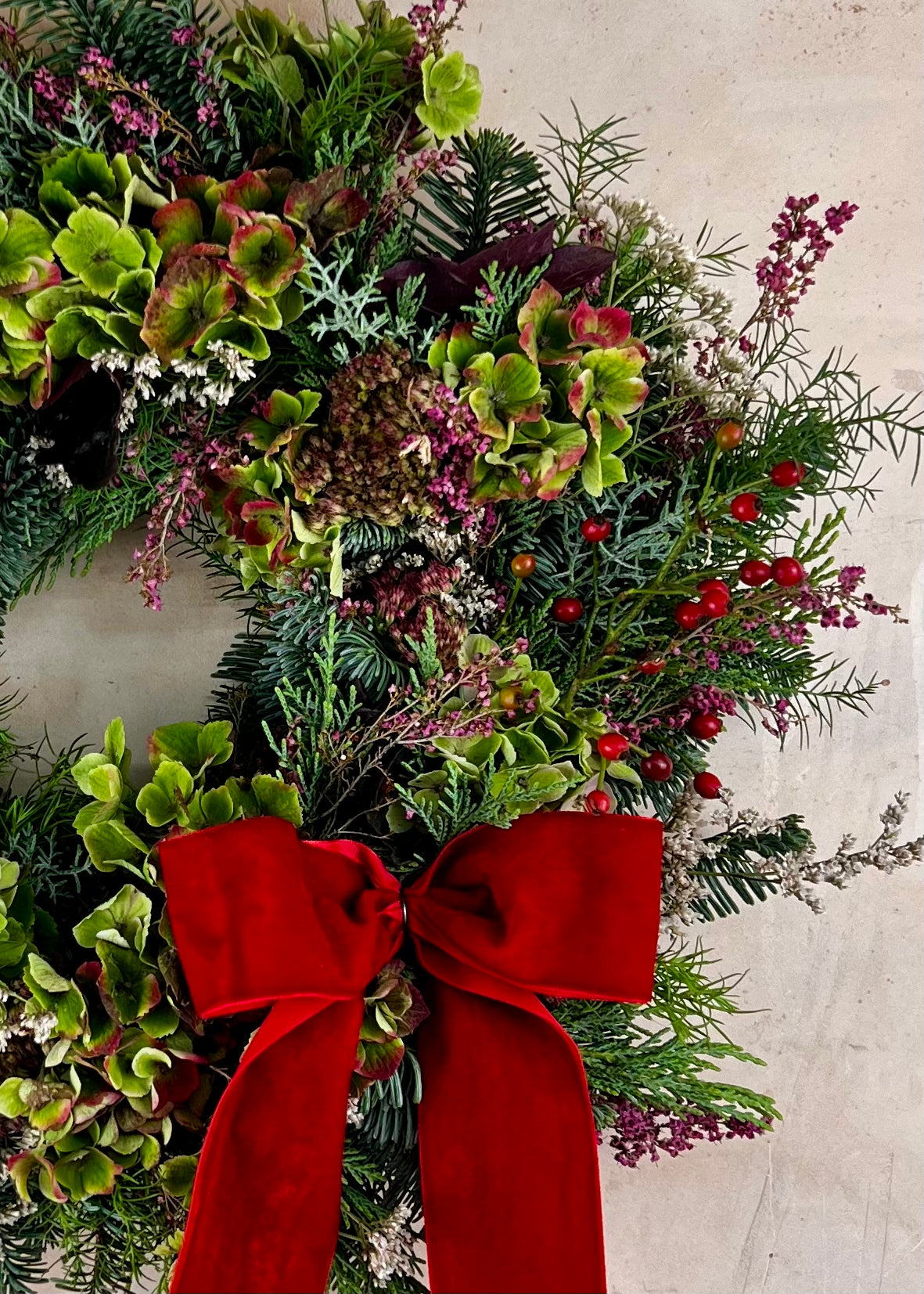 Christmas wreath with greenery, red berries, and a large red bow on a light background