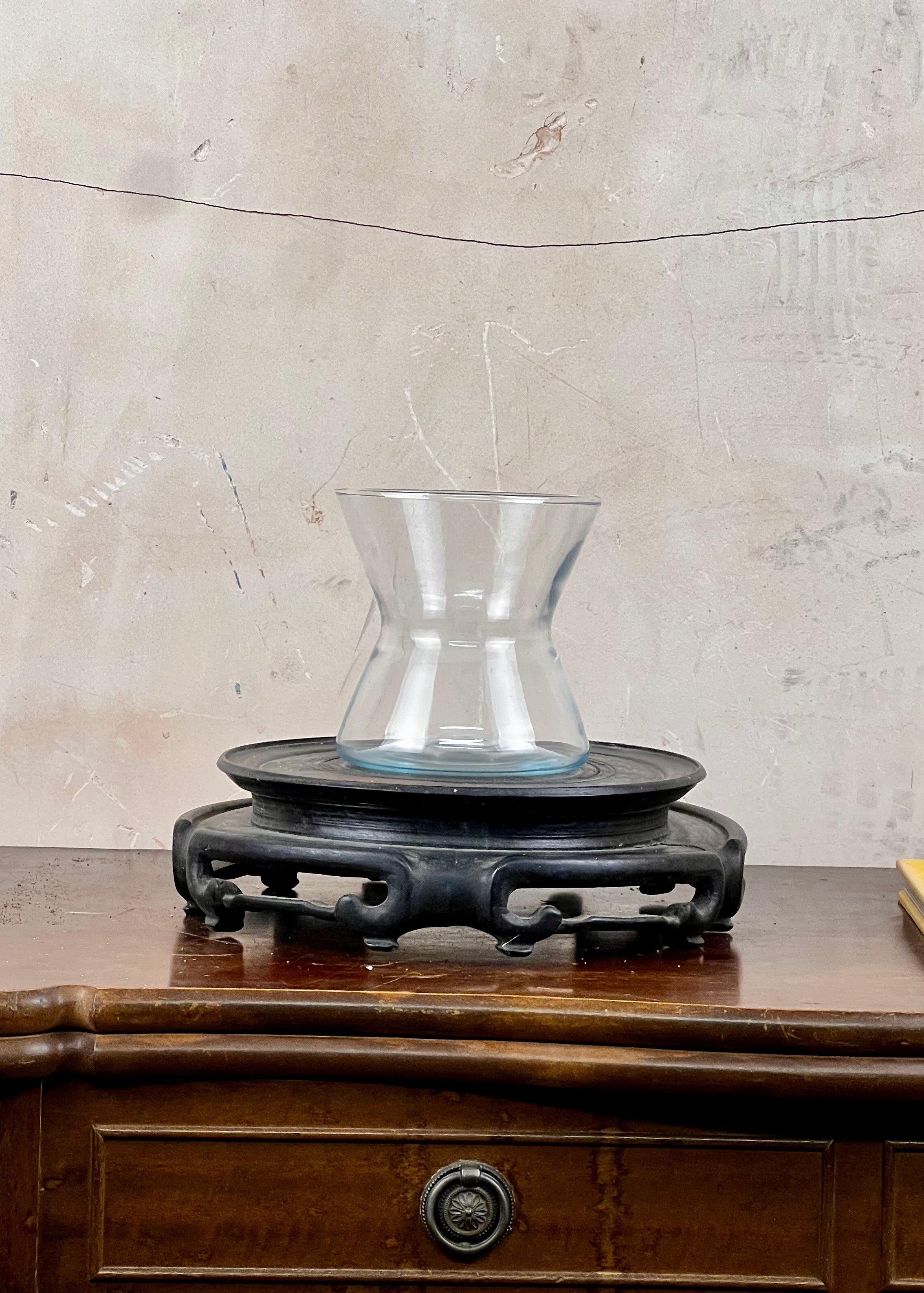 Clear glass vase on a wooden stand against a textured wall.