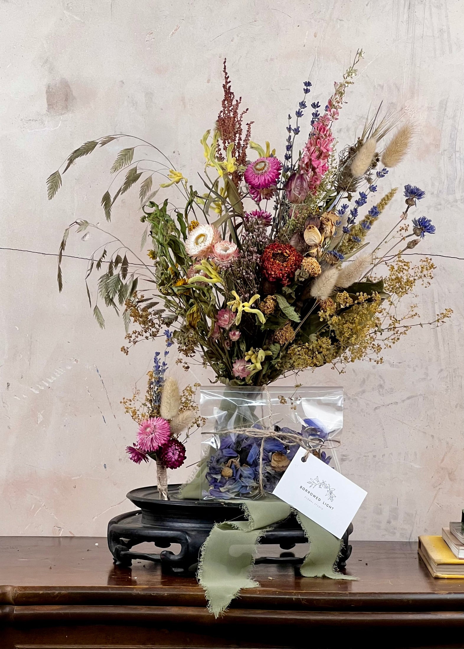 Dried Bridal bouquet of flowers, a matching dried buttonhole and dried confetti on a wooden table with a textured wall background