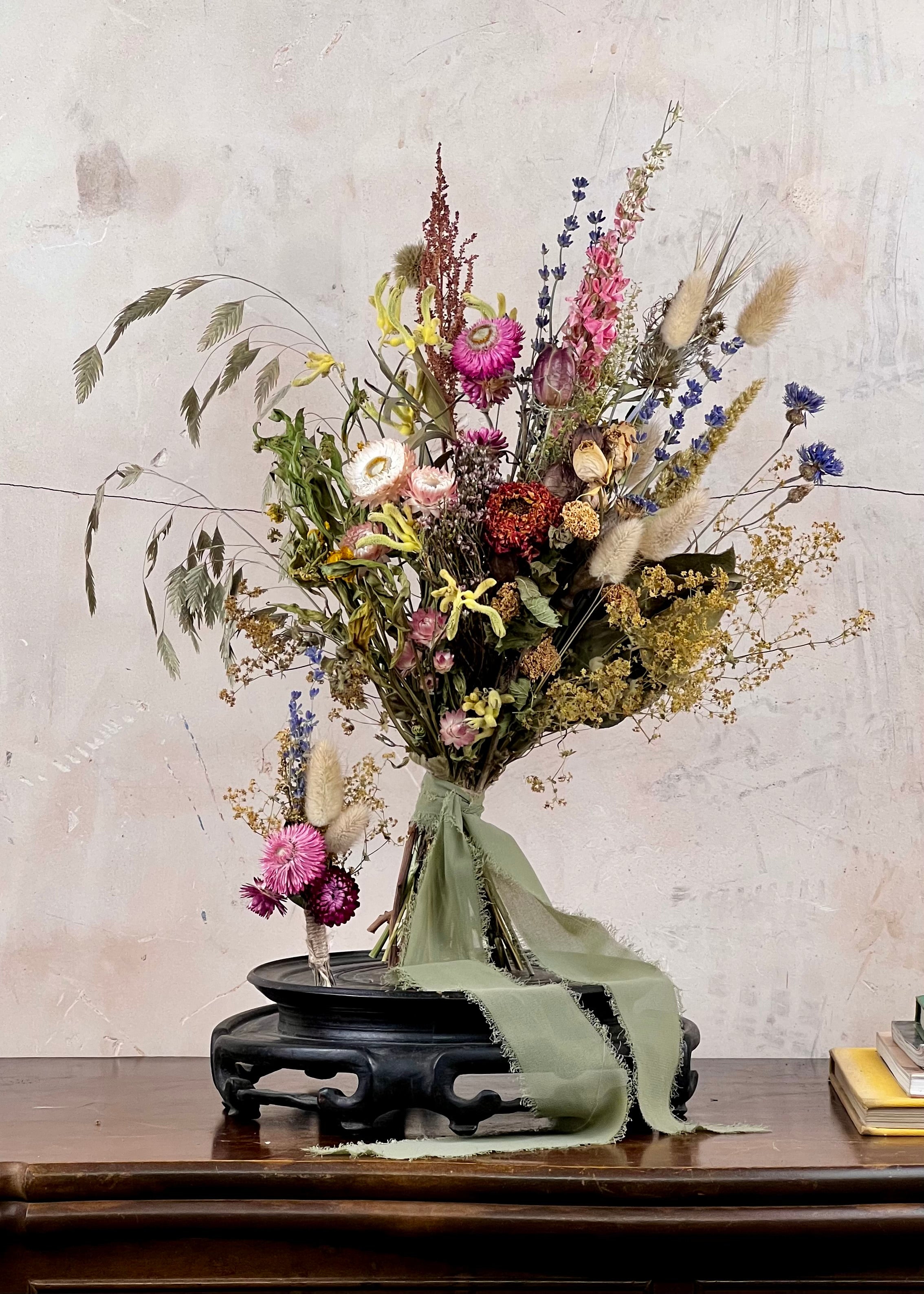 Dried Bridal bouquet of flowers, a matching dried buttonhole on a wooden table with a textured wall background