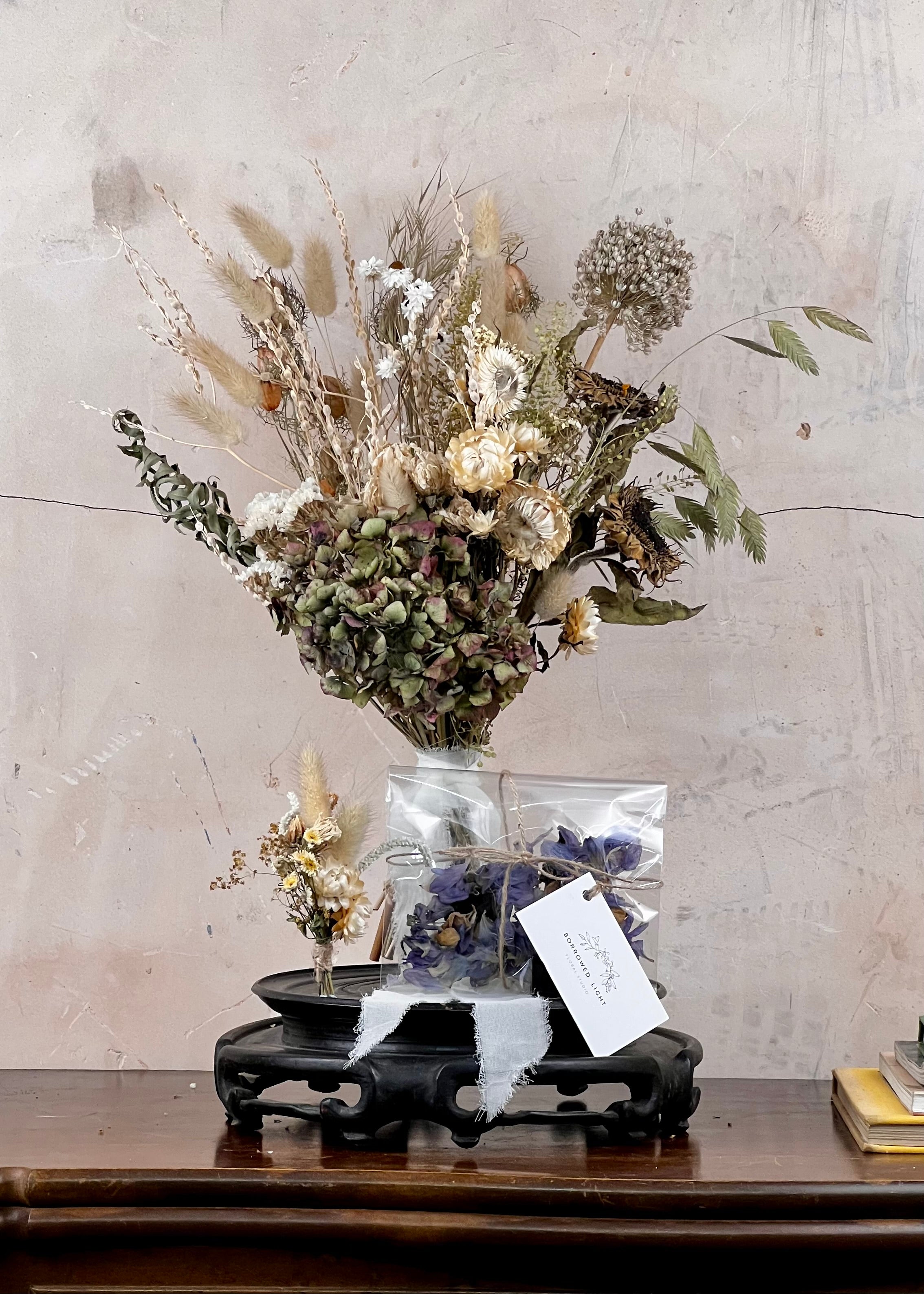 Dried Bridal bouquet of flowers, a matching dried buttonhole and dried confetti on a wooden table with a textured wall background