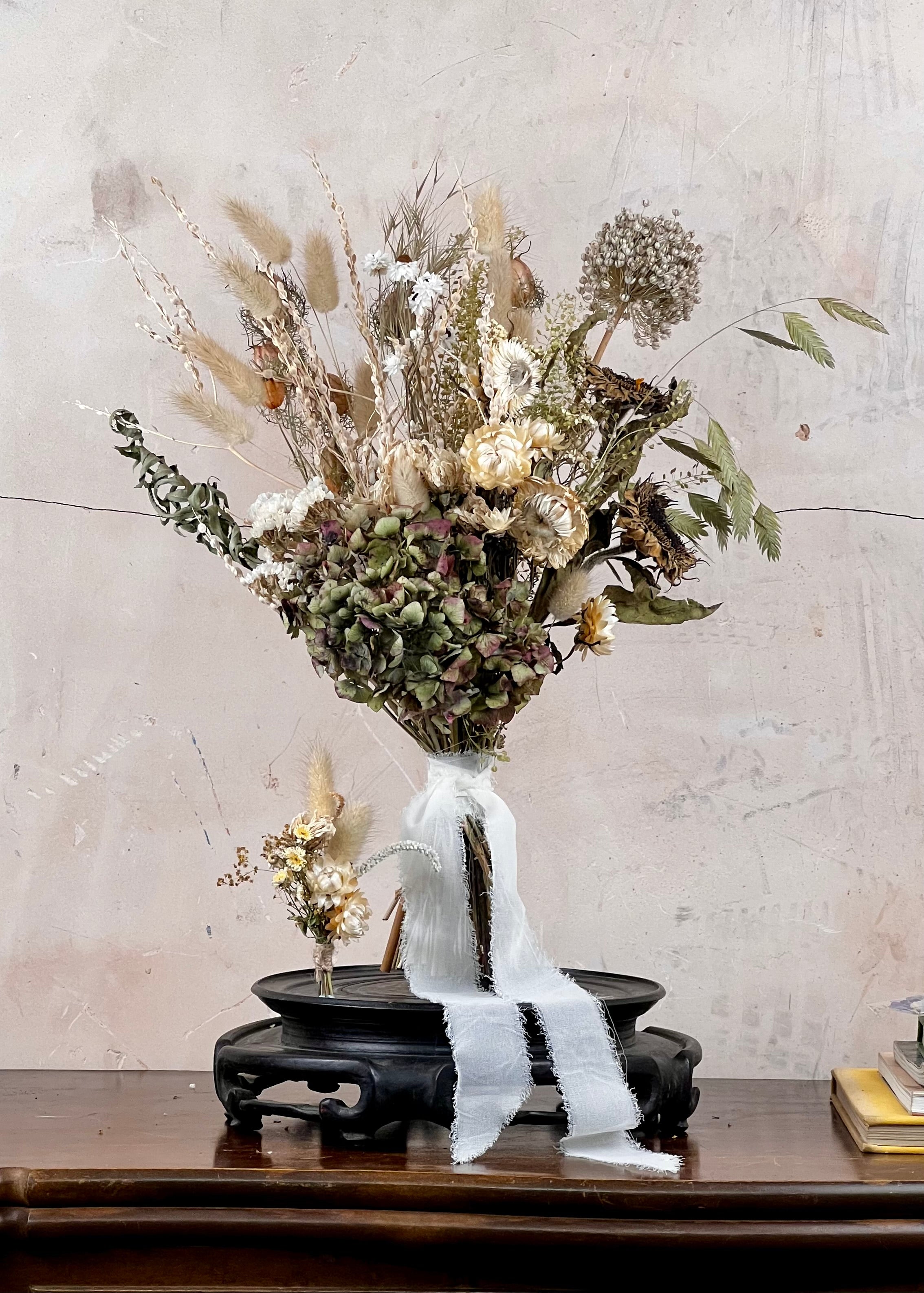 Dried Bridal bouquet of flowers, a matching dried buttonhole on a wooden table with a textured wall background