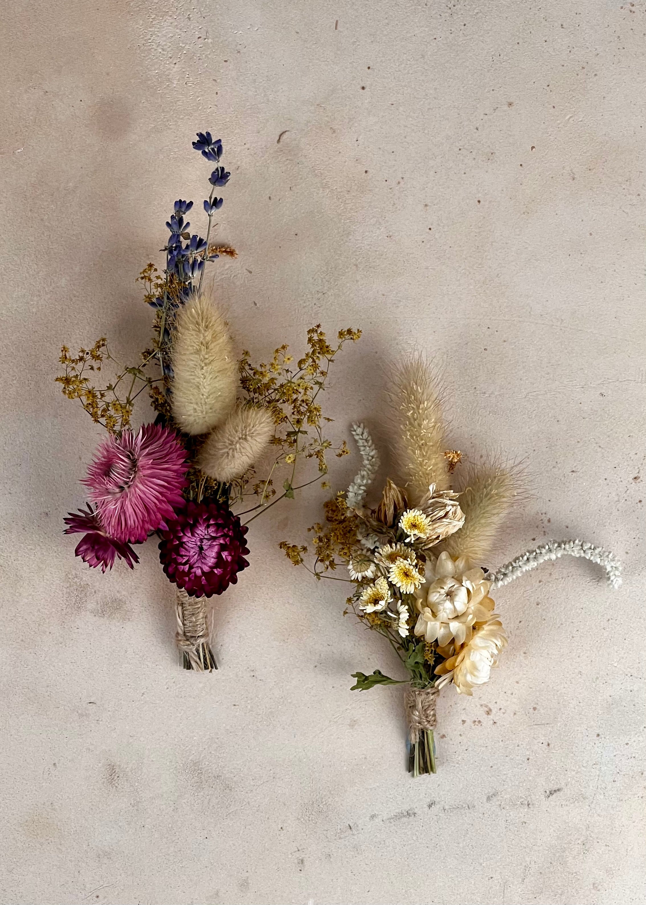 Two dried flower buttonholes on a textured surface