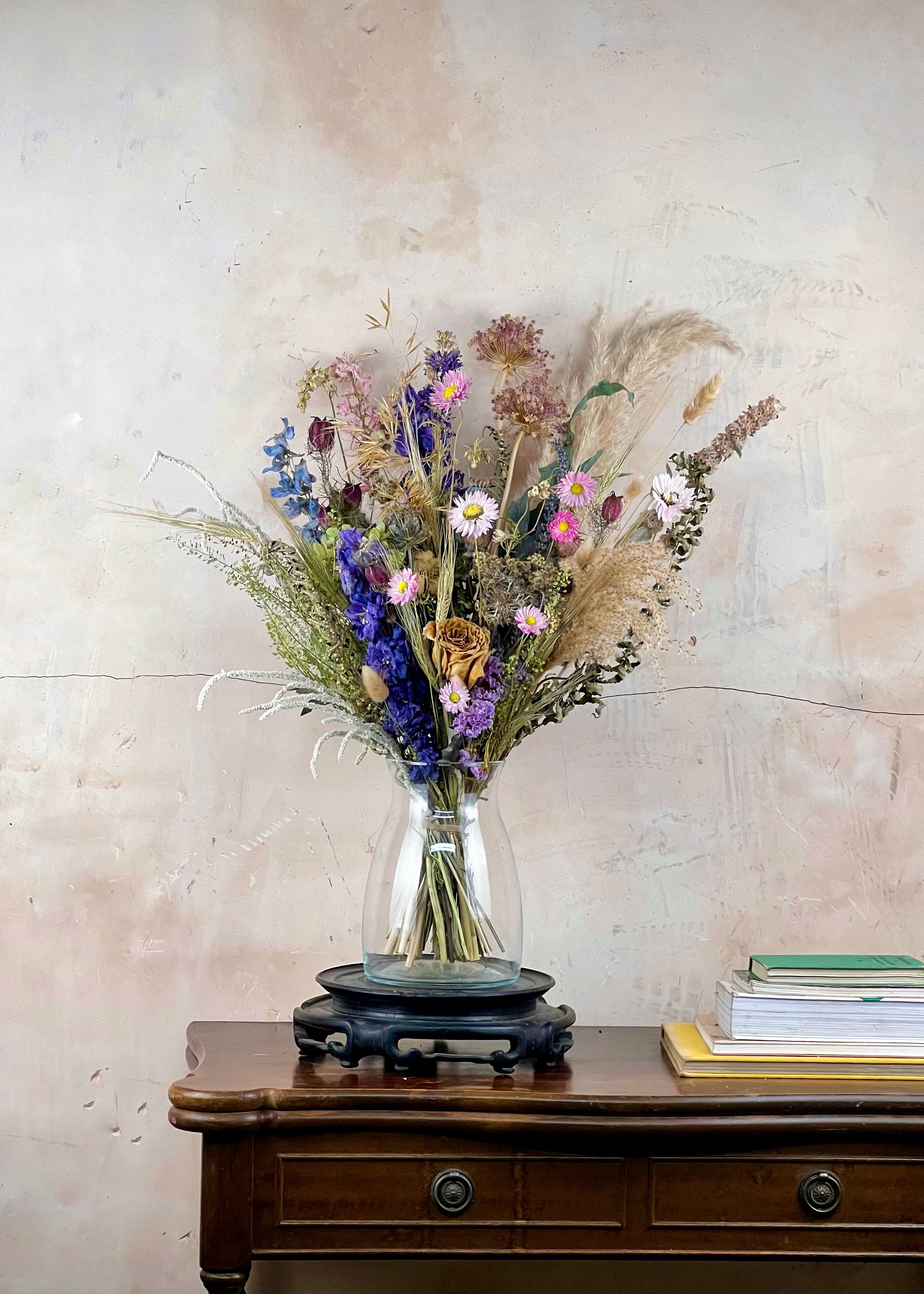 Bouquet of dried flowers in a clear vase on a wooden table against a textured wall.