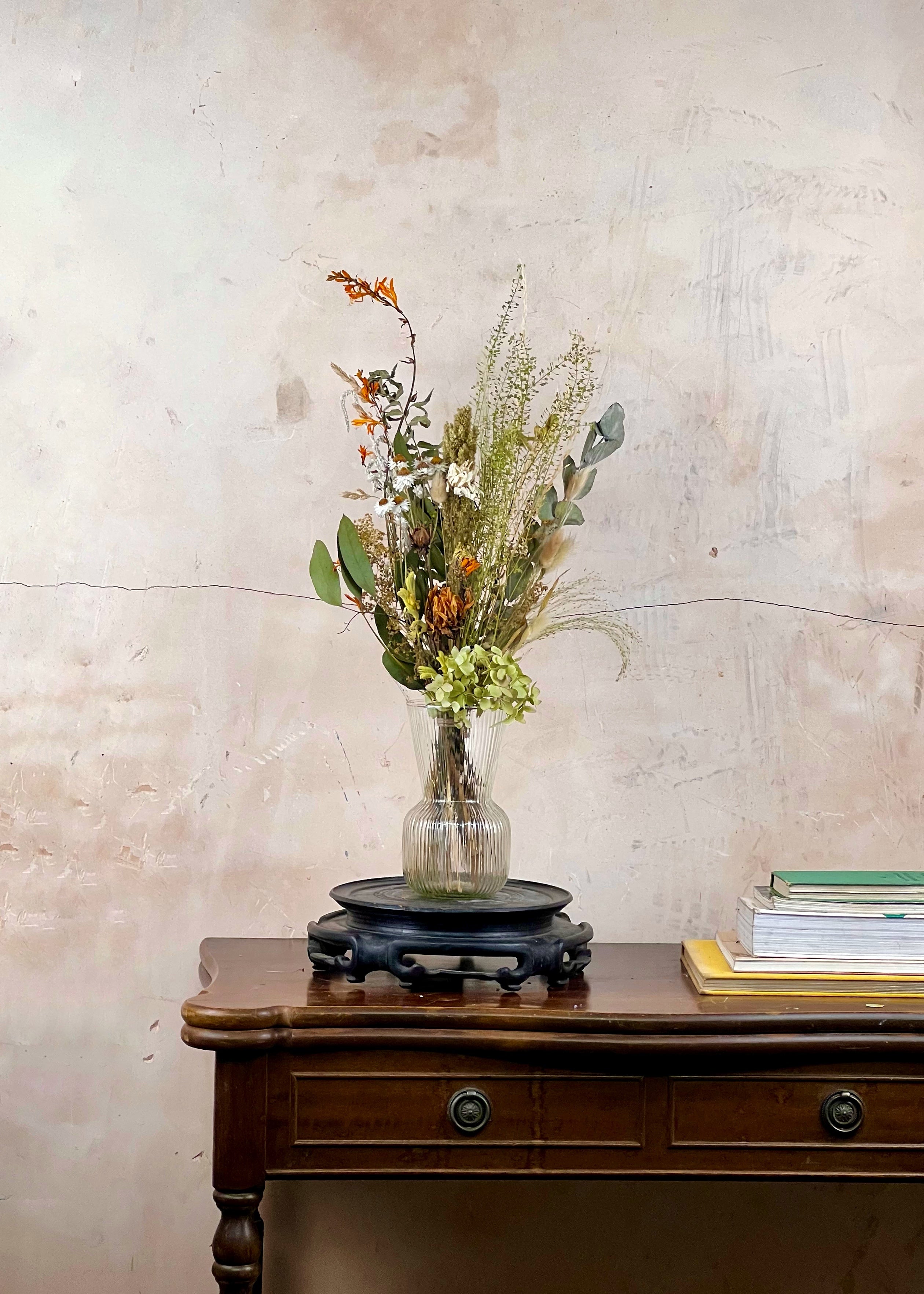 Vase with dried flowers on a wooden table against a textured wall