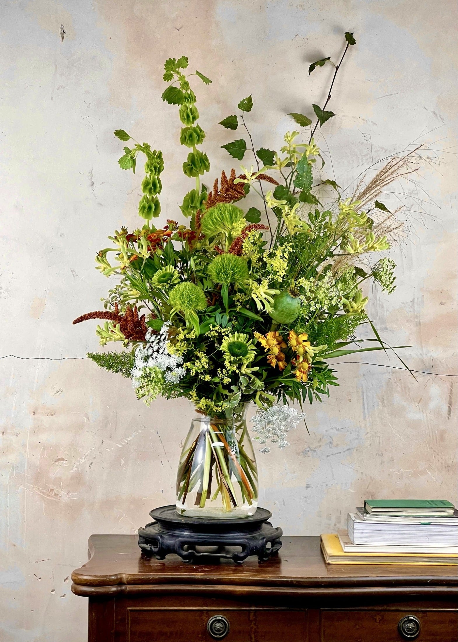 Seasonal Bouquet of flowers and greenery in a clear vase on a wooden table with a light background