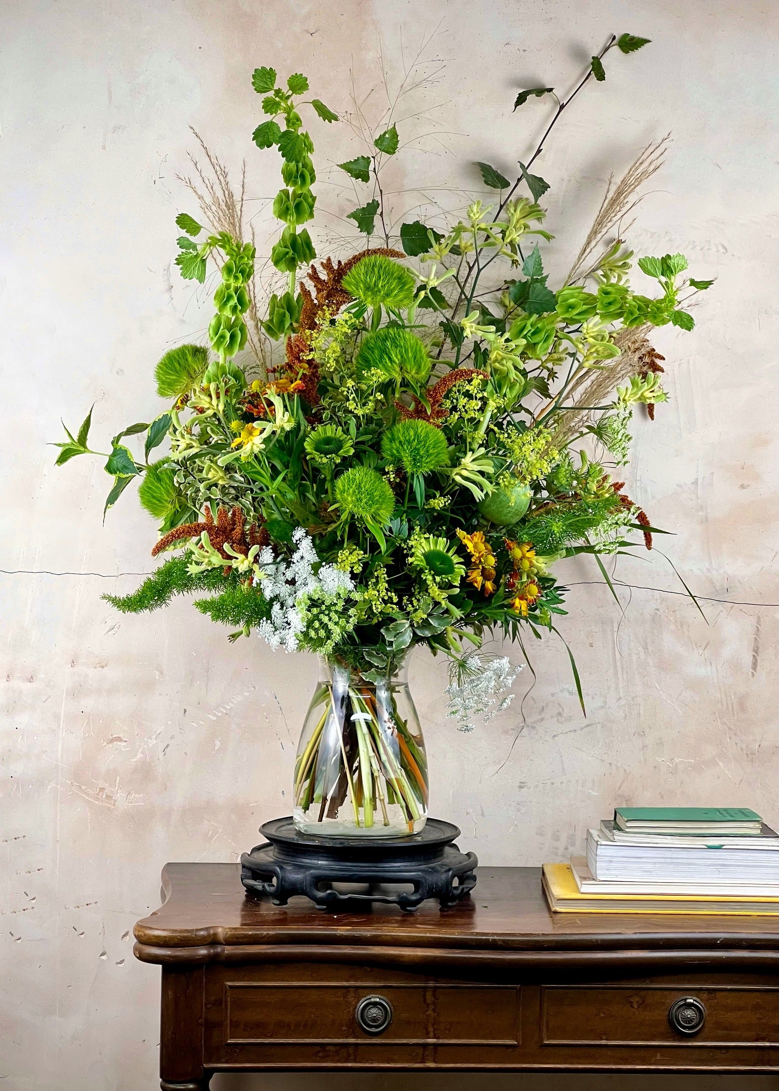 Seasonal Bouquet of flowers and greenery in a clear vase on a wooden table with a light background