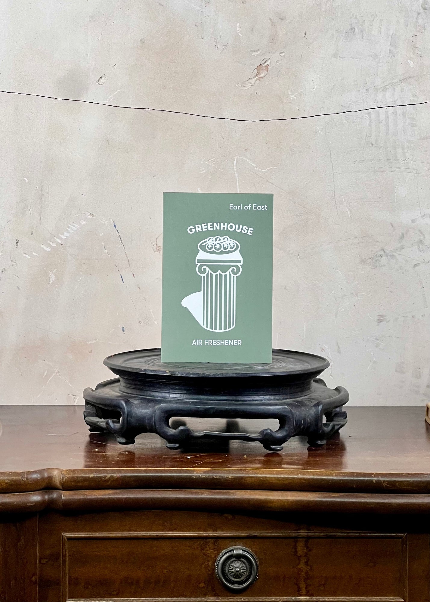 Green air freshener packaging on a wooden surface with a textured wall background