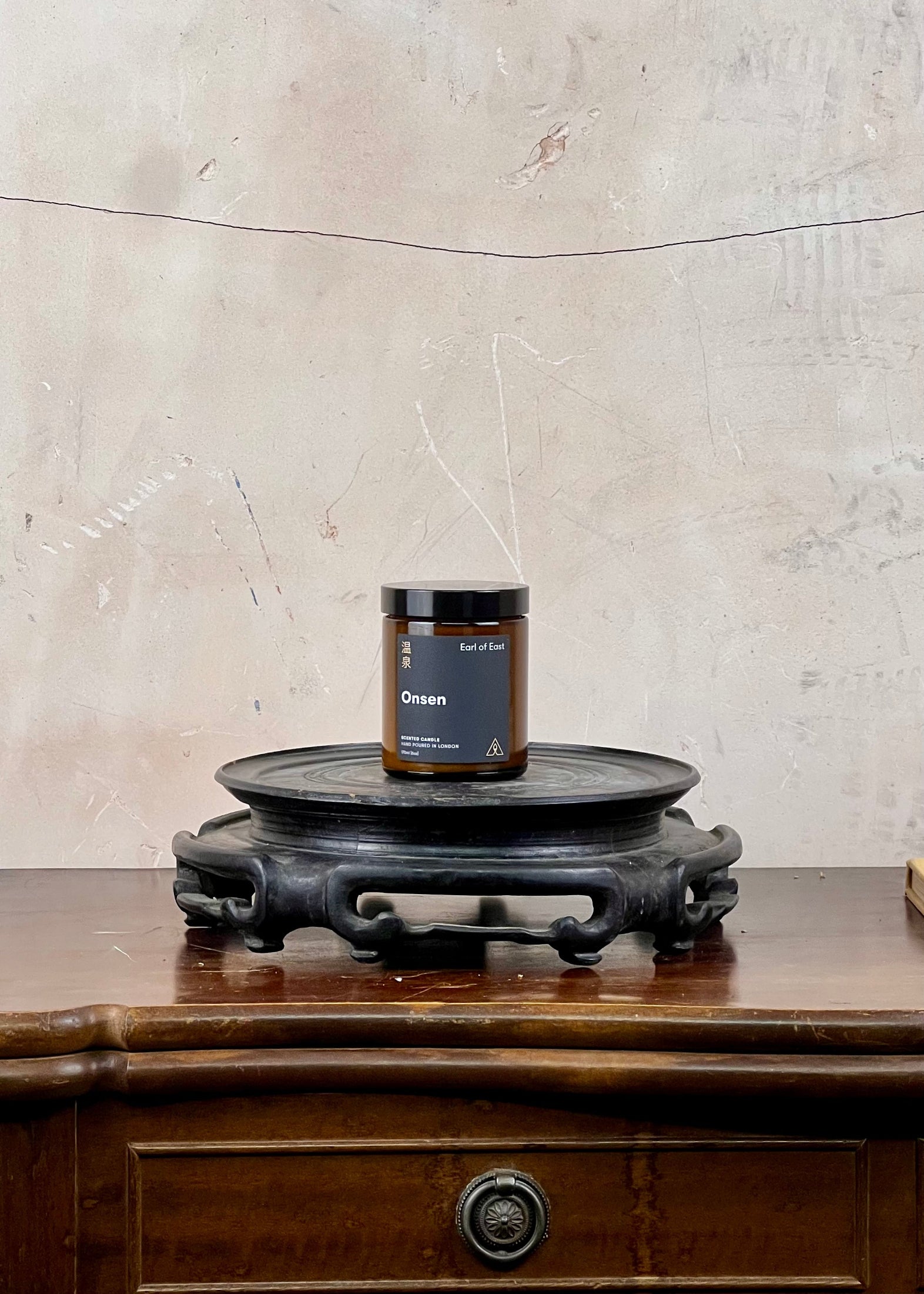 Candle on a wooden stand against a textured wall.