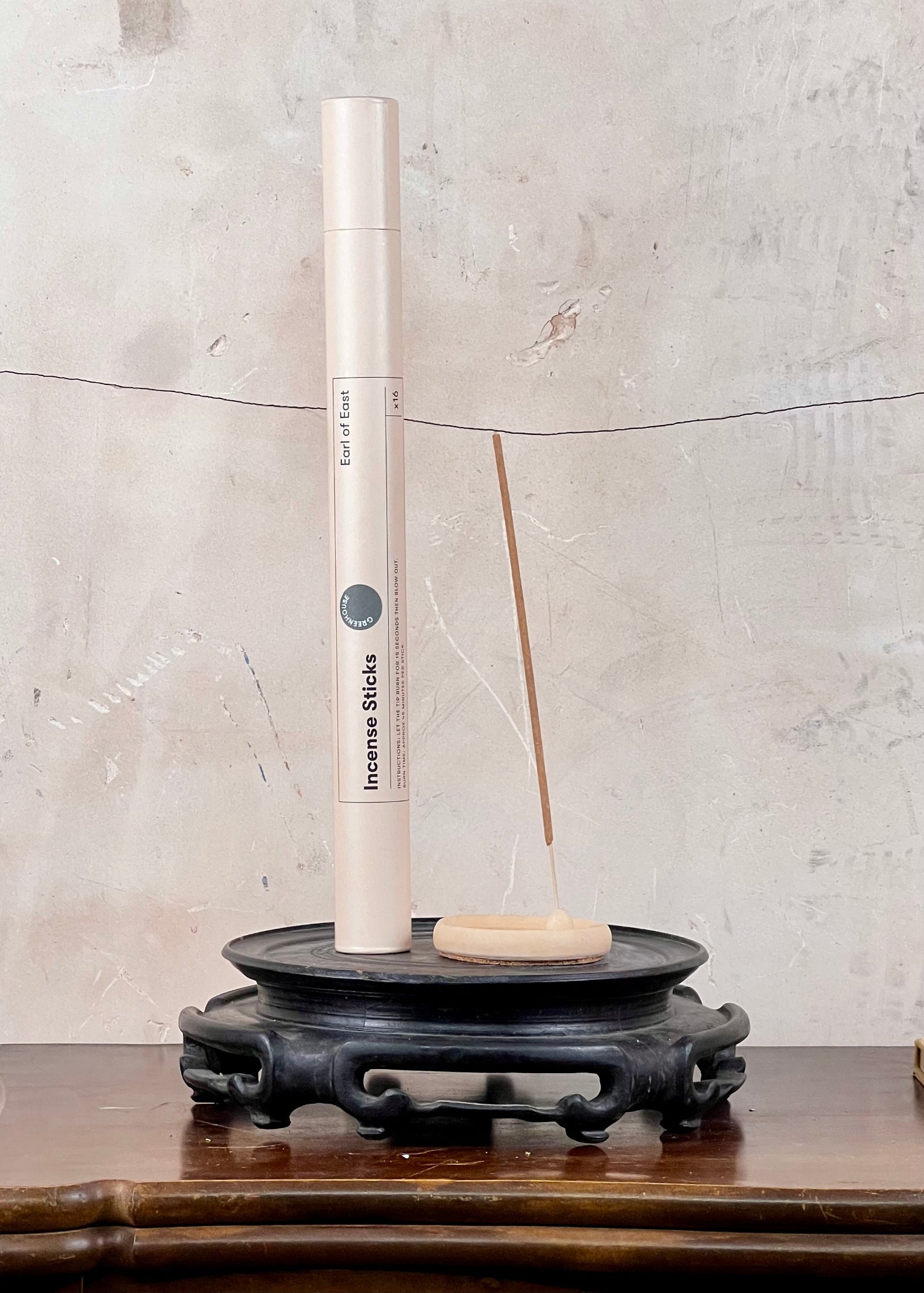 Incense stick holder with incense sticks on a wooden surface against a textured wall.