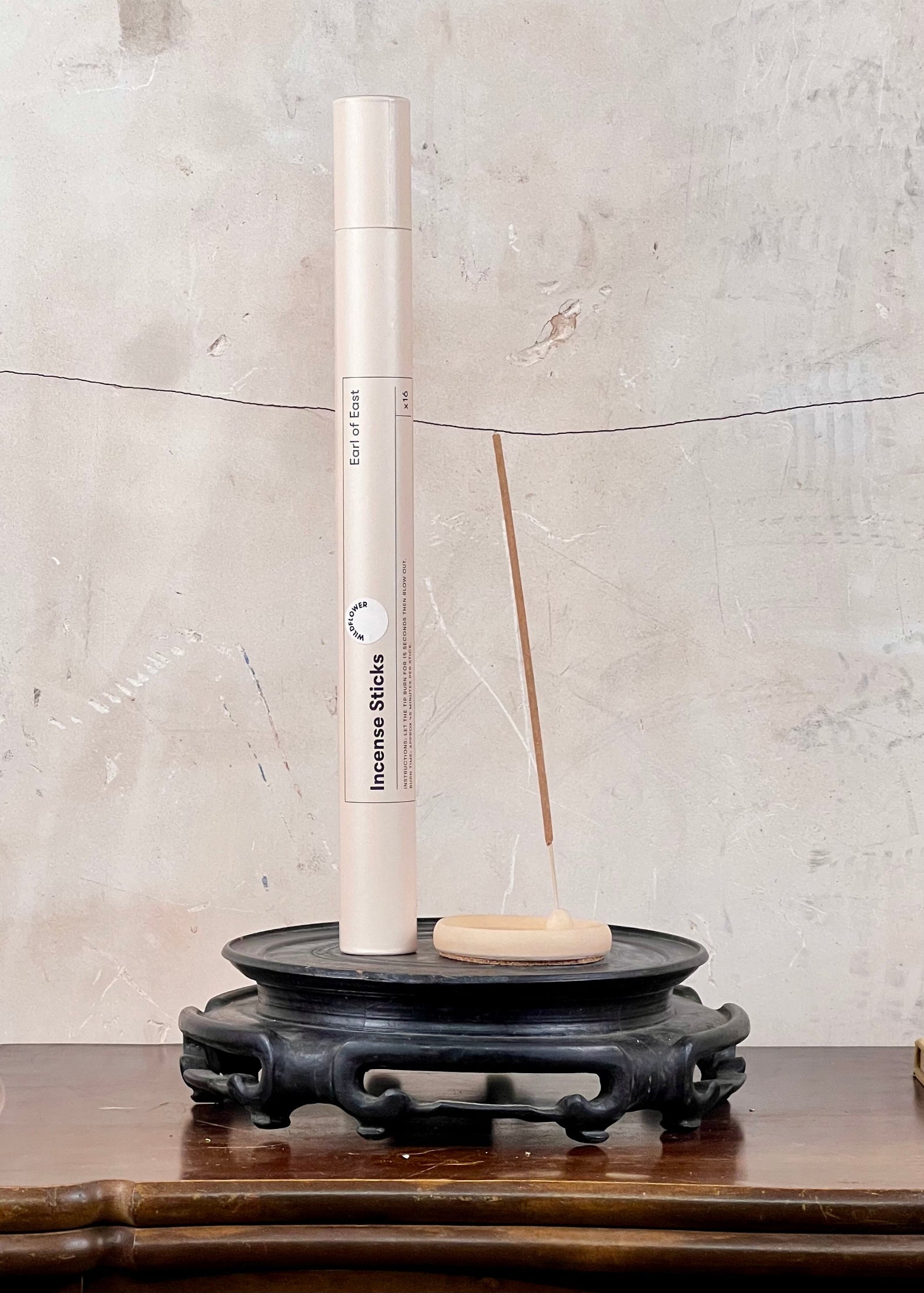 Incense stick holder with incense sticks on a wooden surface against a textured wall.