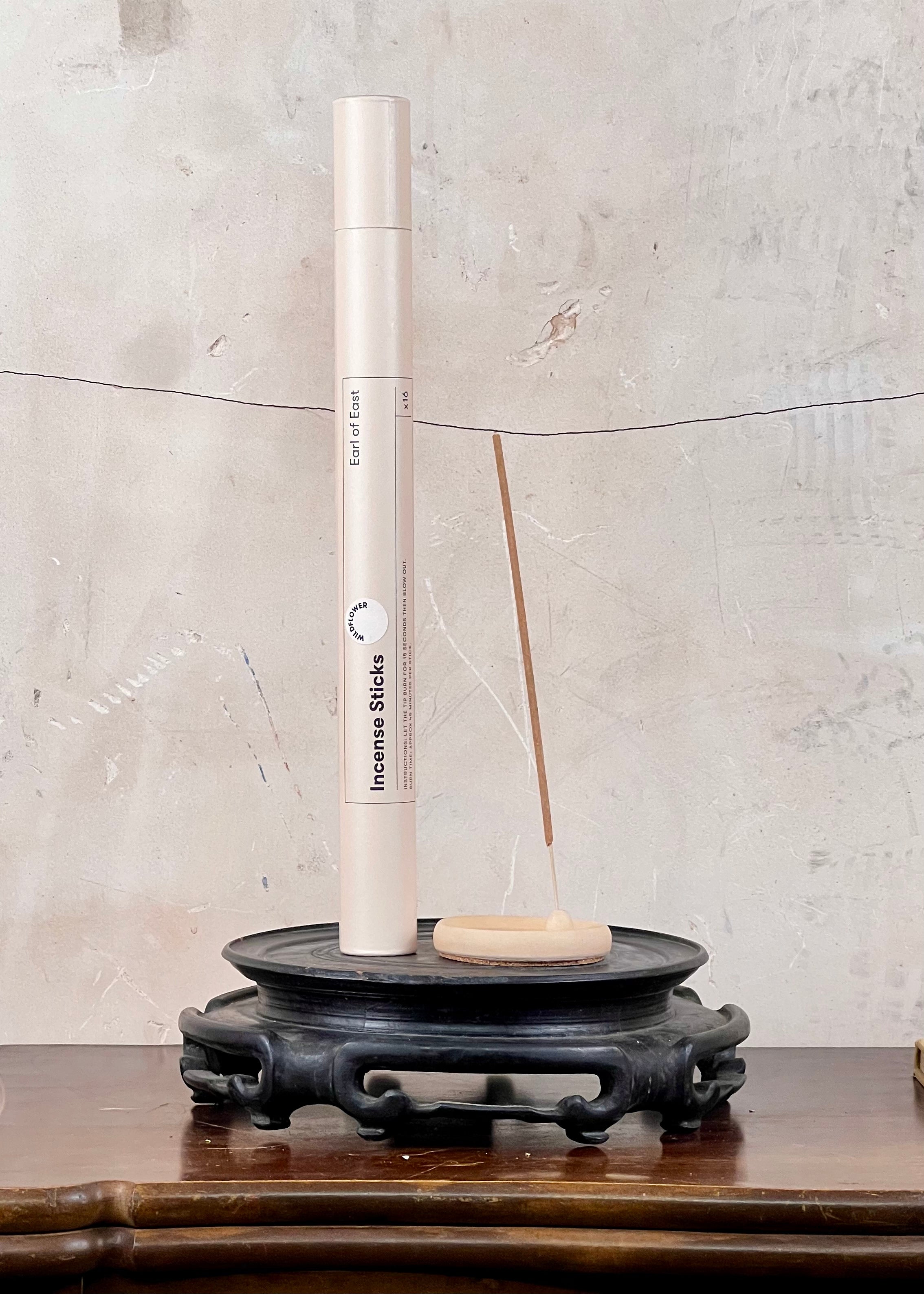 Incense stick holder with incense sticks on a wooden surface against a textured wall.