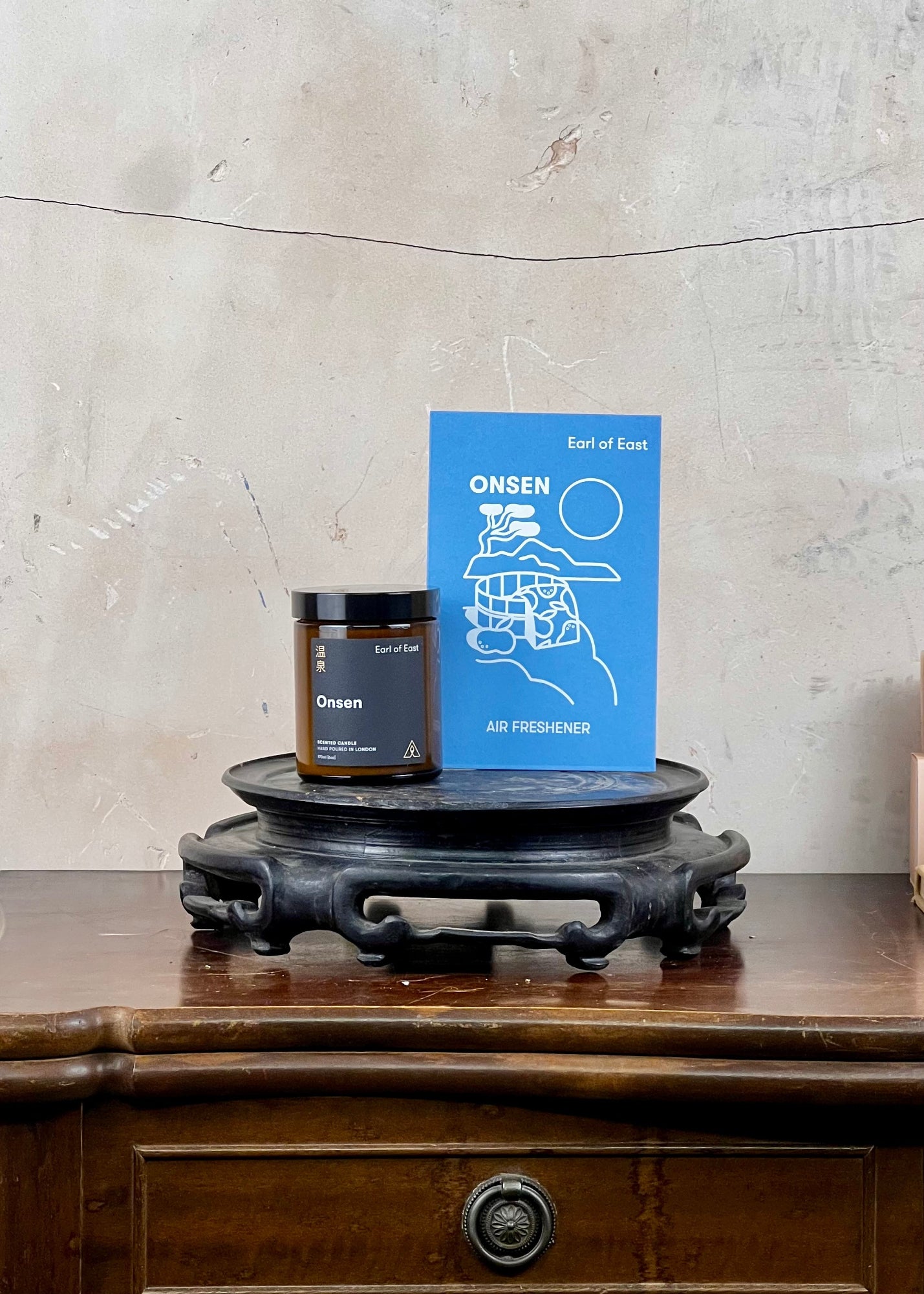 Onsen air freshener and candle set with a  a wooden surface against a concrete wall.