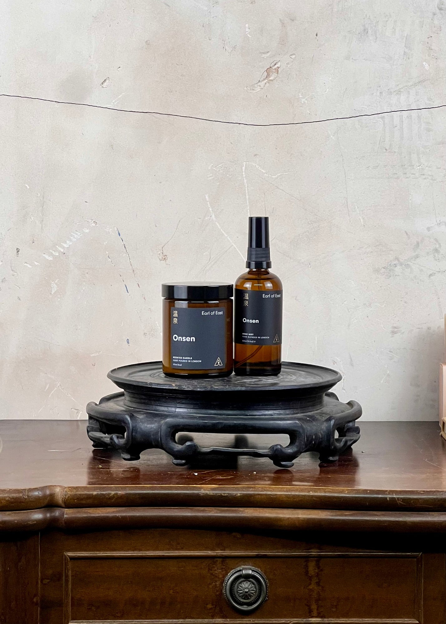 Earl of East Onsen candle and spray mist on a wooden stand against a textured wall.